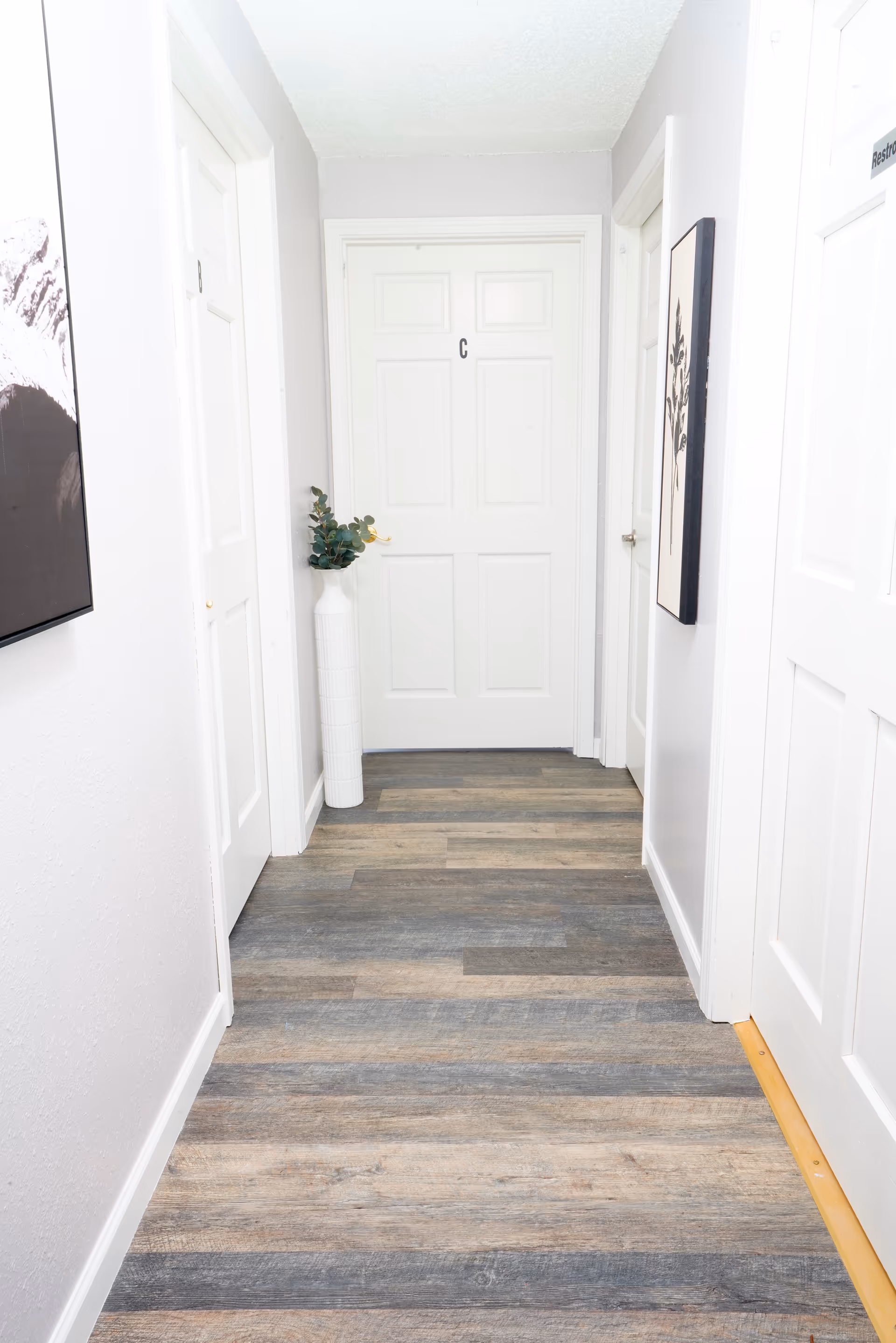 Bright hallway in a senior living facility with closed doors and a tall white vase.