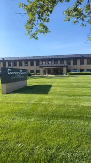 Exterior view of a two-story facility with a sign reading Corporate Square on a green lawn.