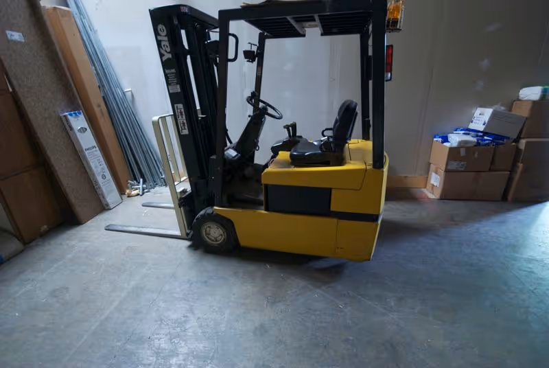 Yellow forklift parked inside a cluttered warehouse with boxes and supplies.