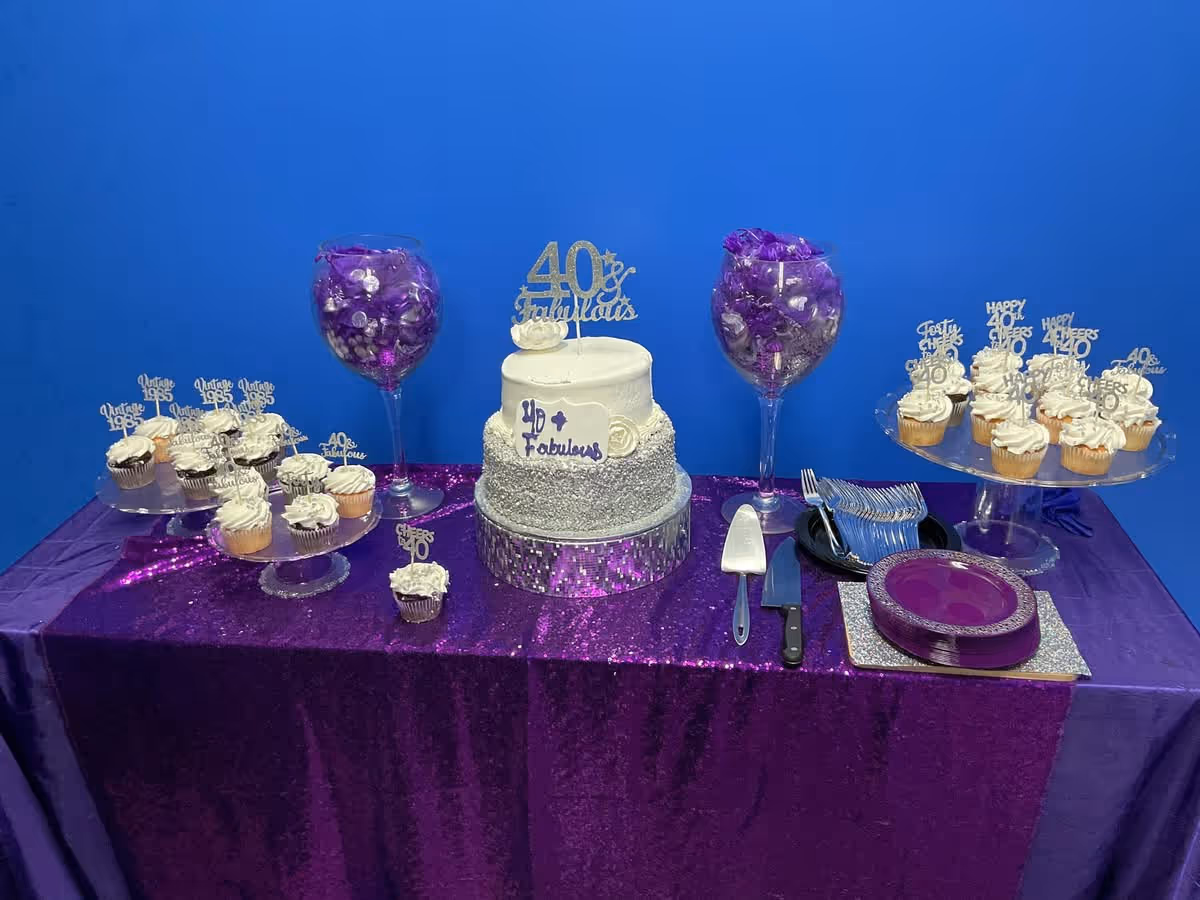 Table with cake and cupcakes on a purple-draped table against a blue wall.