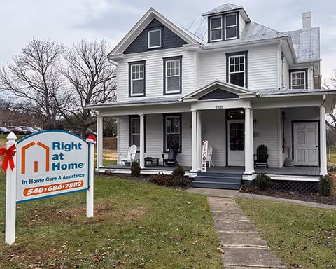A white two-story house-style facility with a front porch and a Right at Home sign.