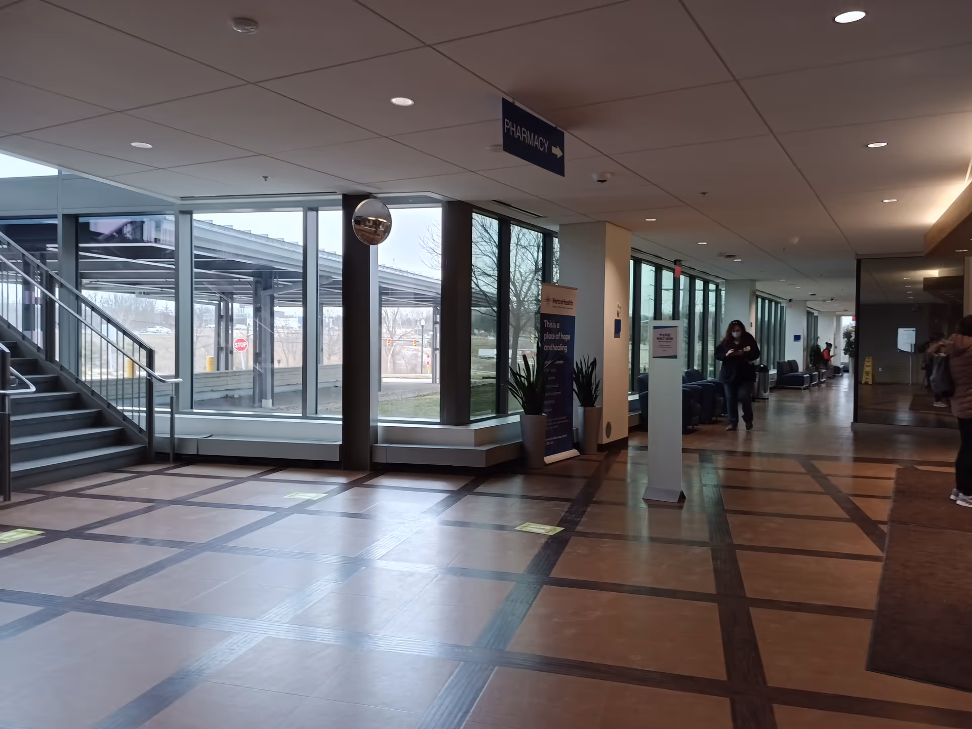 Wide hospital-like lobby with large windows, a staircase, seating, and pharmacy sign.