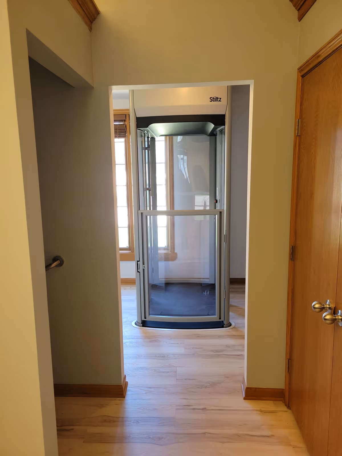 Interior hallway with a Stiltz residential elevator at the end and wooden floors.