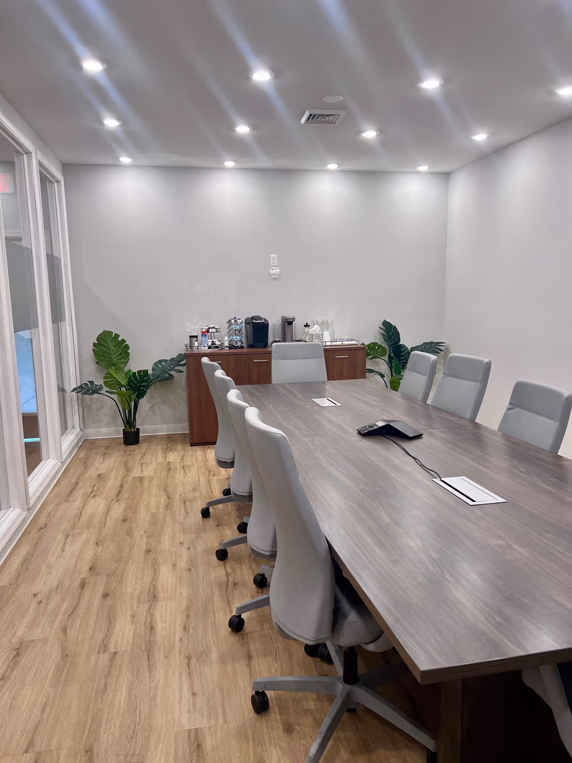 Long conference table with gray chairs in a modern meeting room, coffee station against back wall.