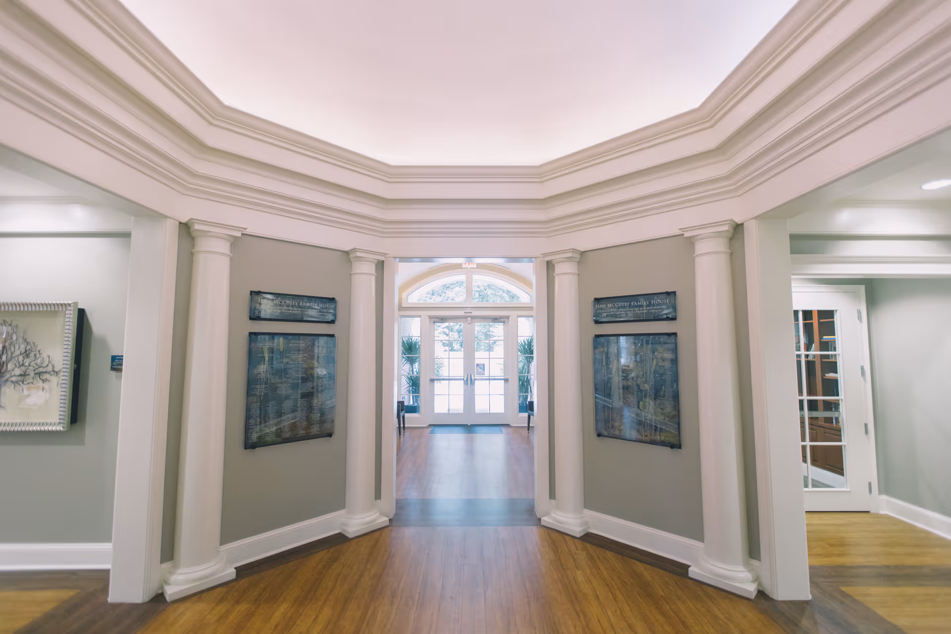 Bright interior hallway with tall columns, crown molding, and a glass doorway at the far end.