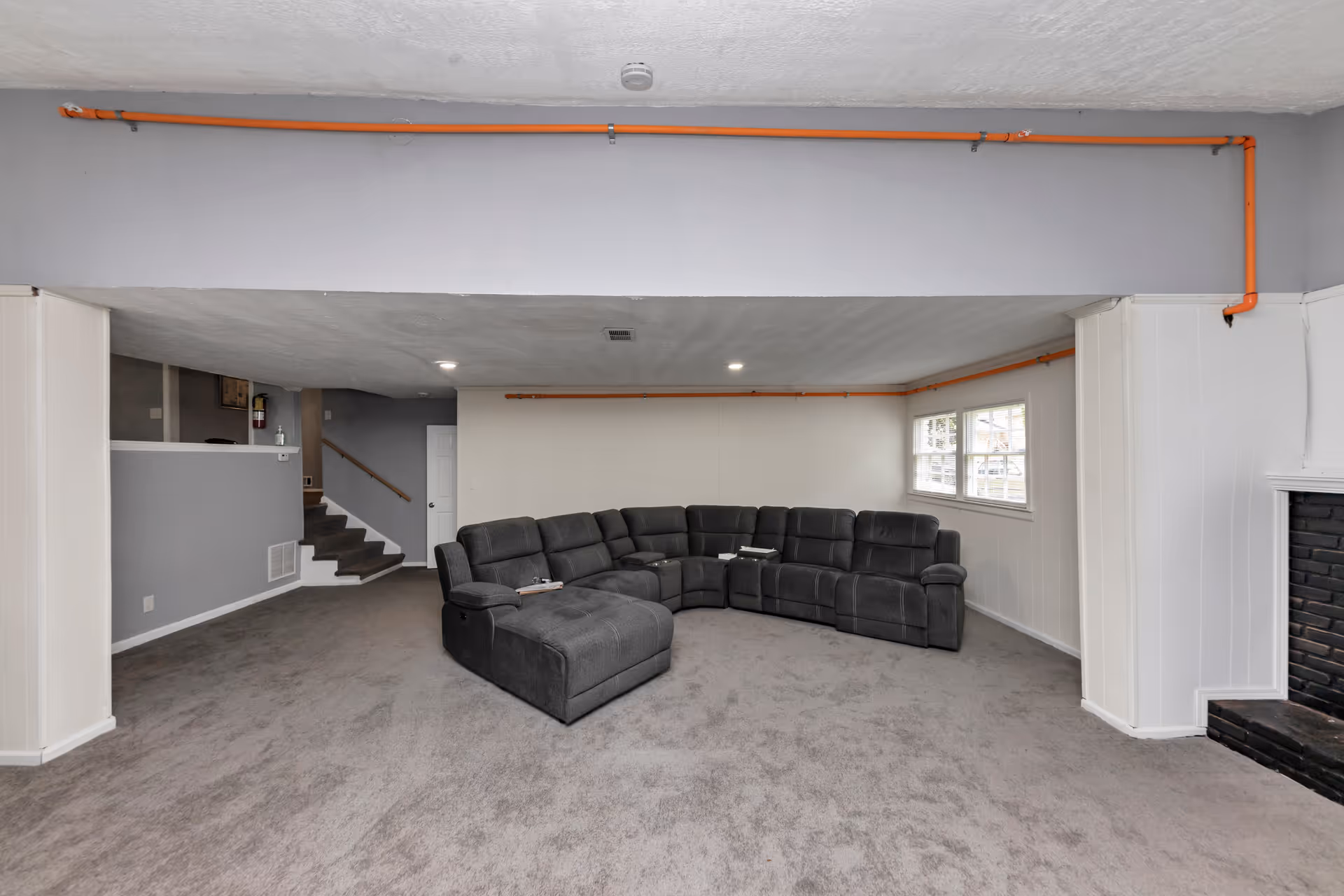 Basement-like living area with a large gray sectional sofa, window, stairs, and fireplace.