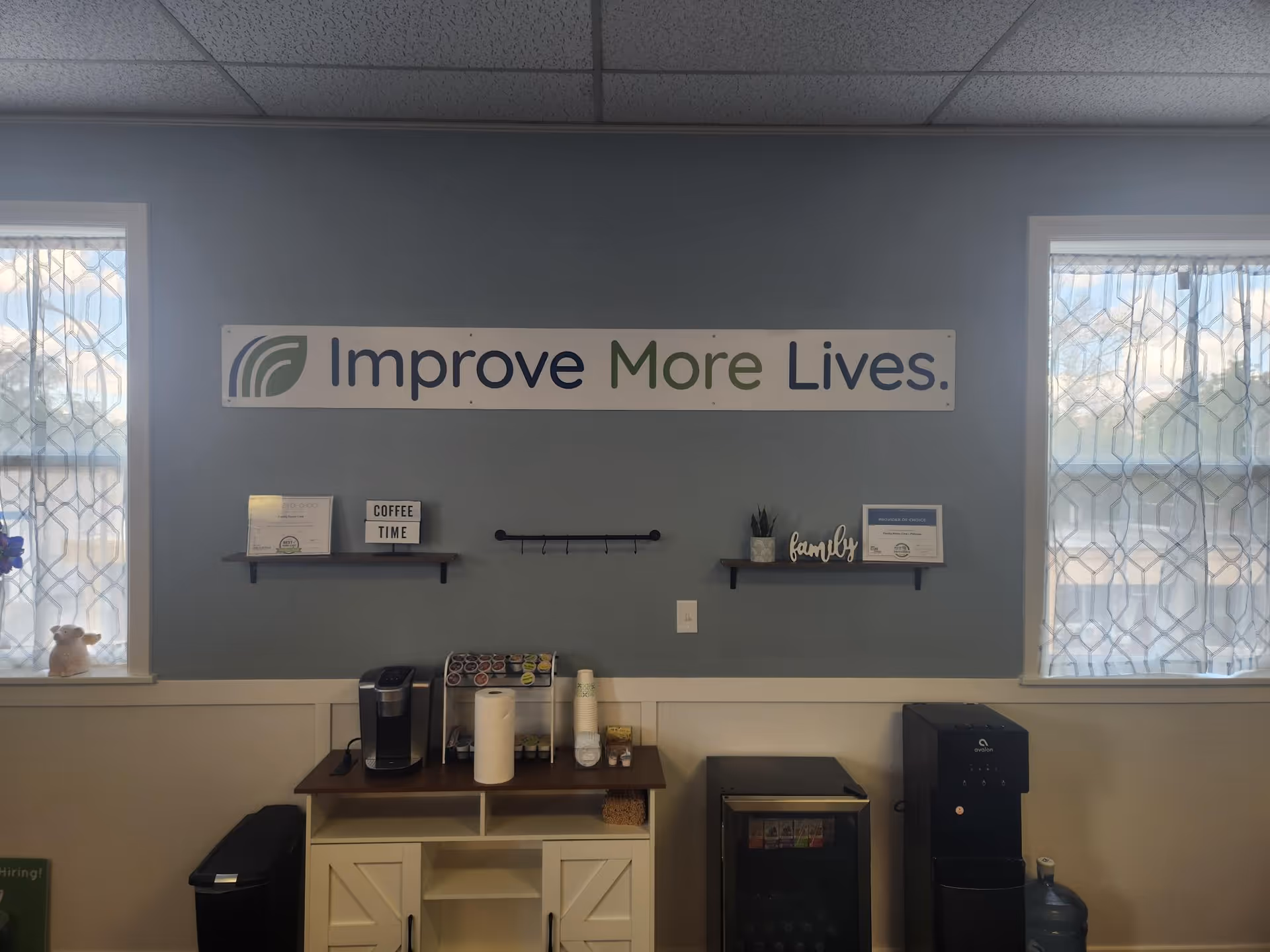 Interior lounge area with coffee station and a sign reading Improve More Lives on blue wall.