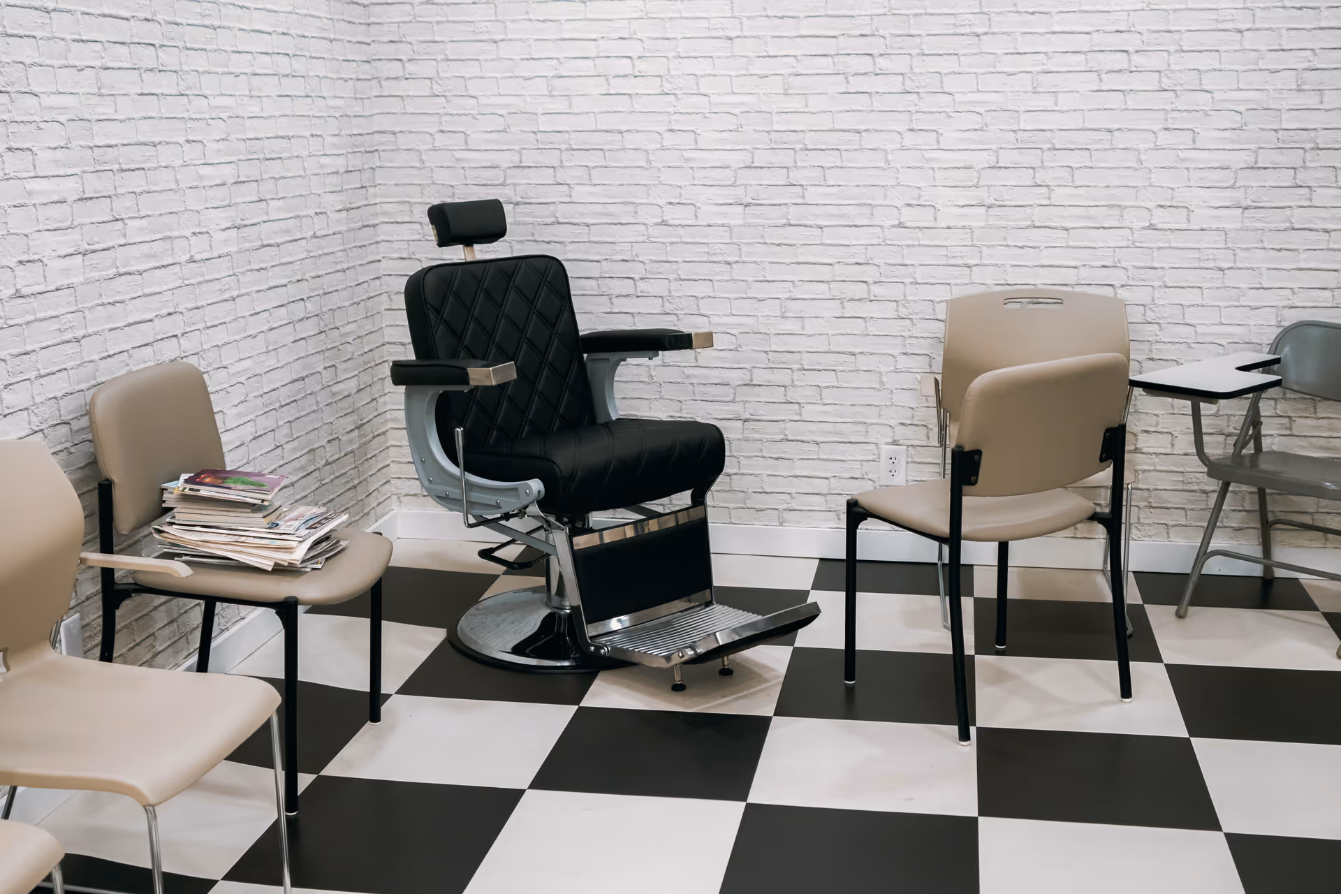 A barber chair sits in a modern waiting area with beige chairs and checkered floor.