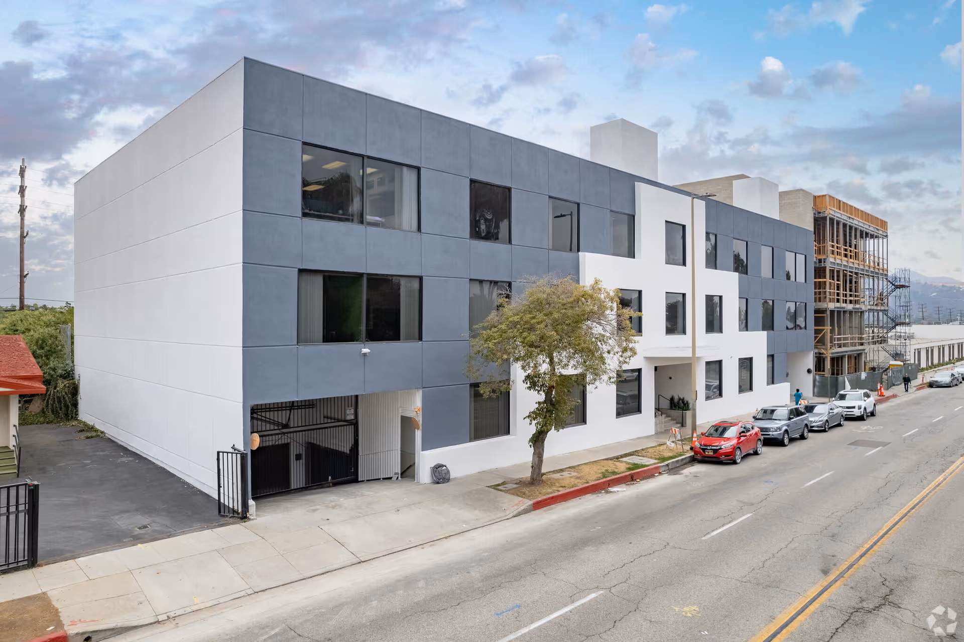 Modern gray-and-white hospice building along a street with parked cars.