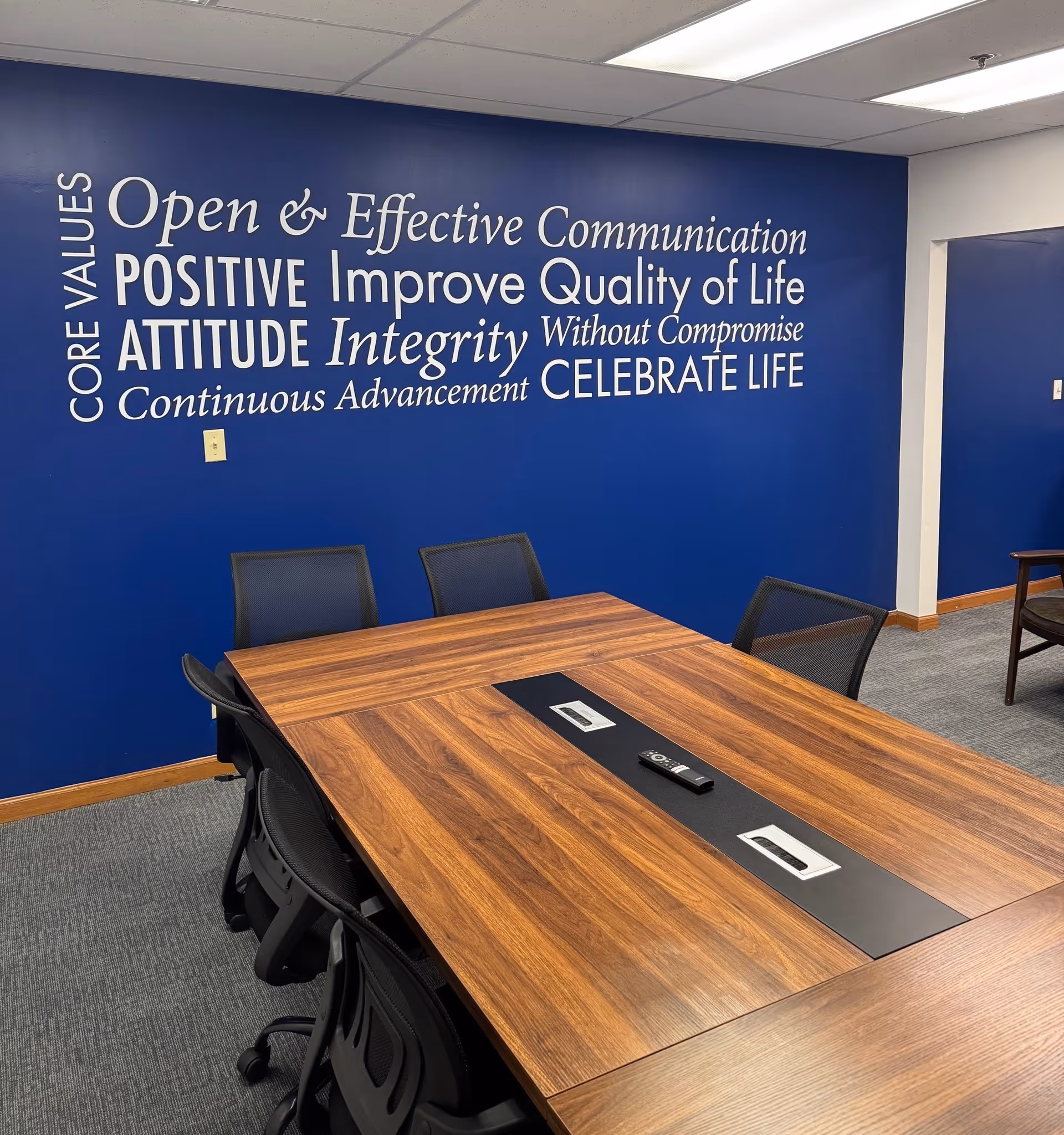 Blue wall conference room with a long wooden table and motivational wall text.