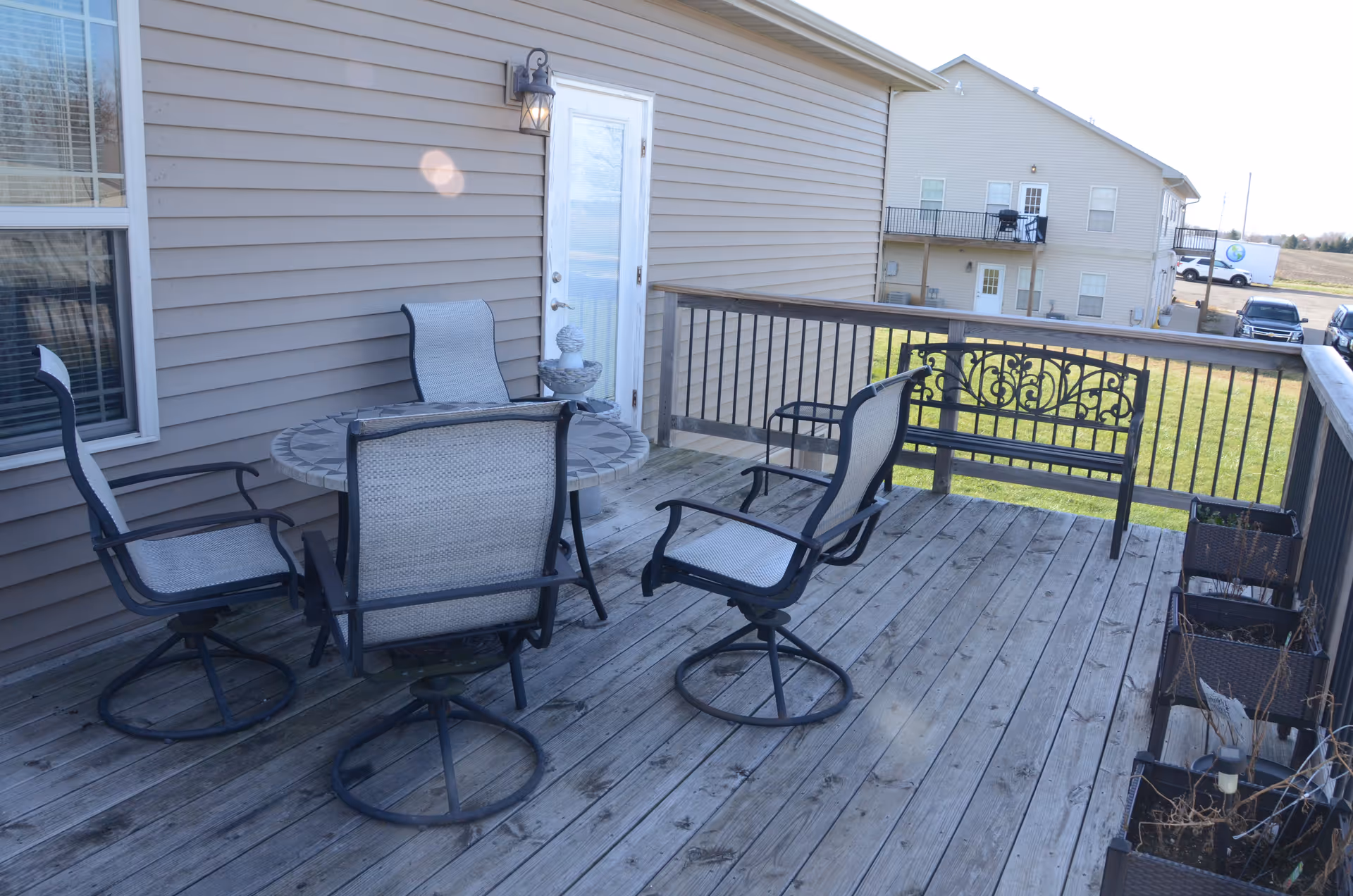 Outdoor wooden deck with a round table and chairs beside a beige building.