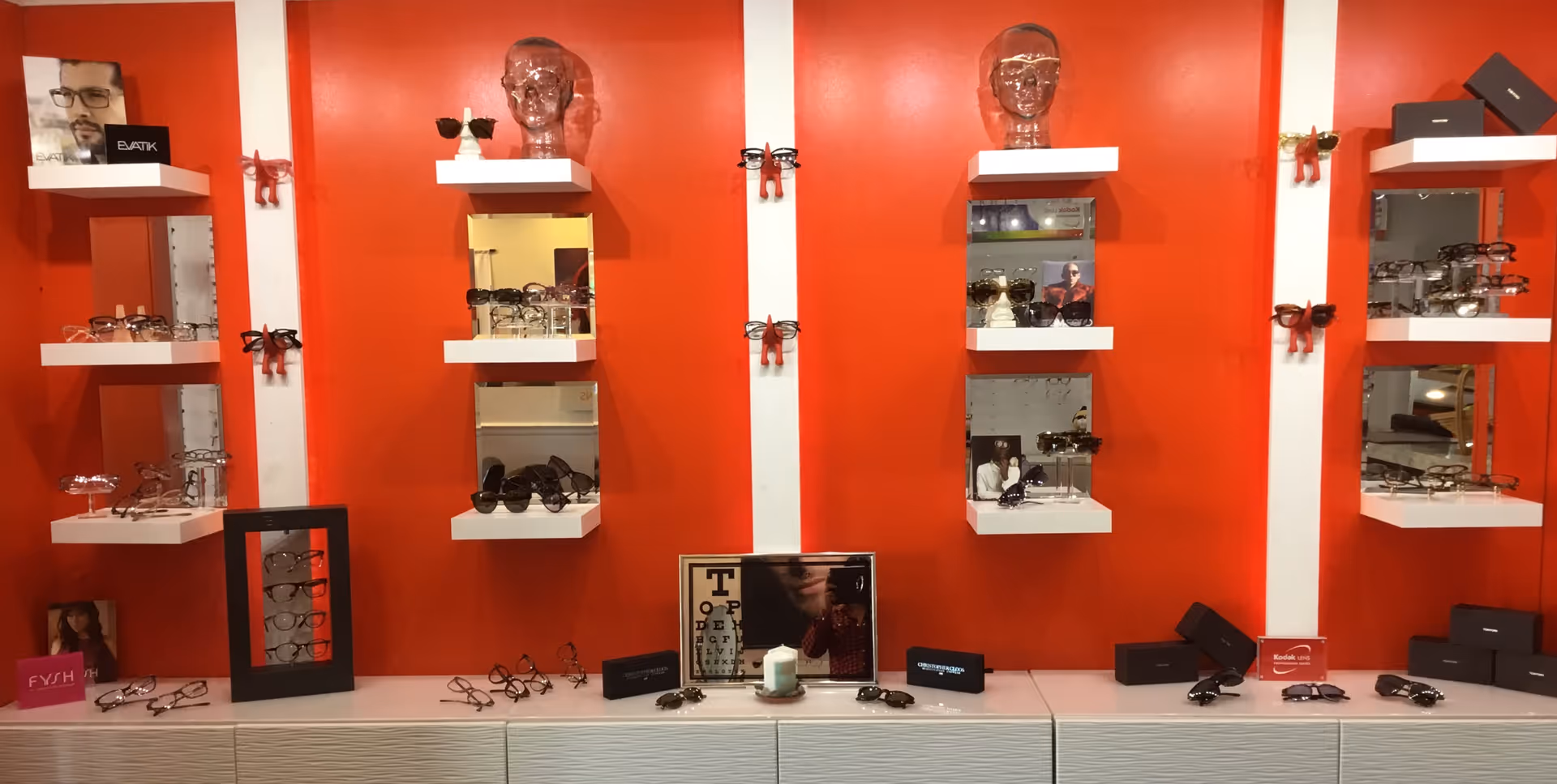 Interior optometry showroom with red walls and white shelves displaying eyeglasses.