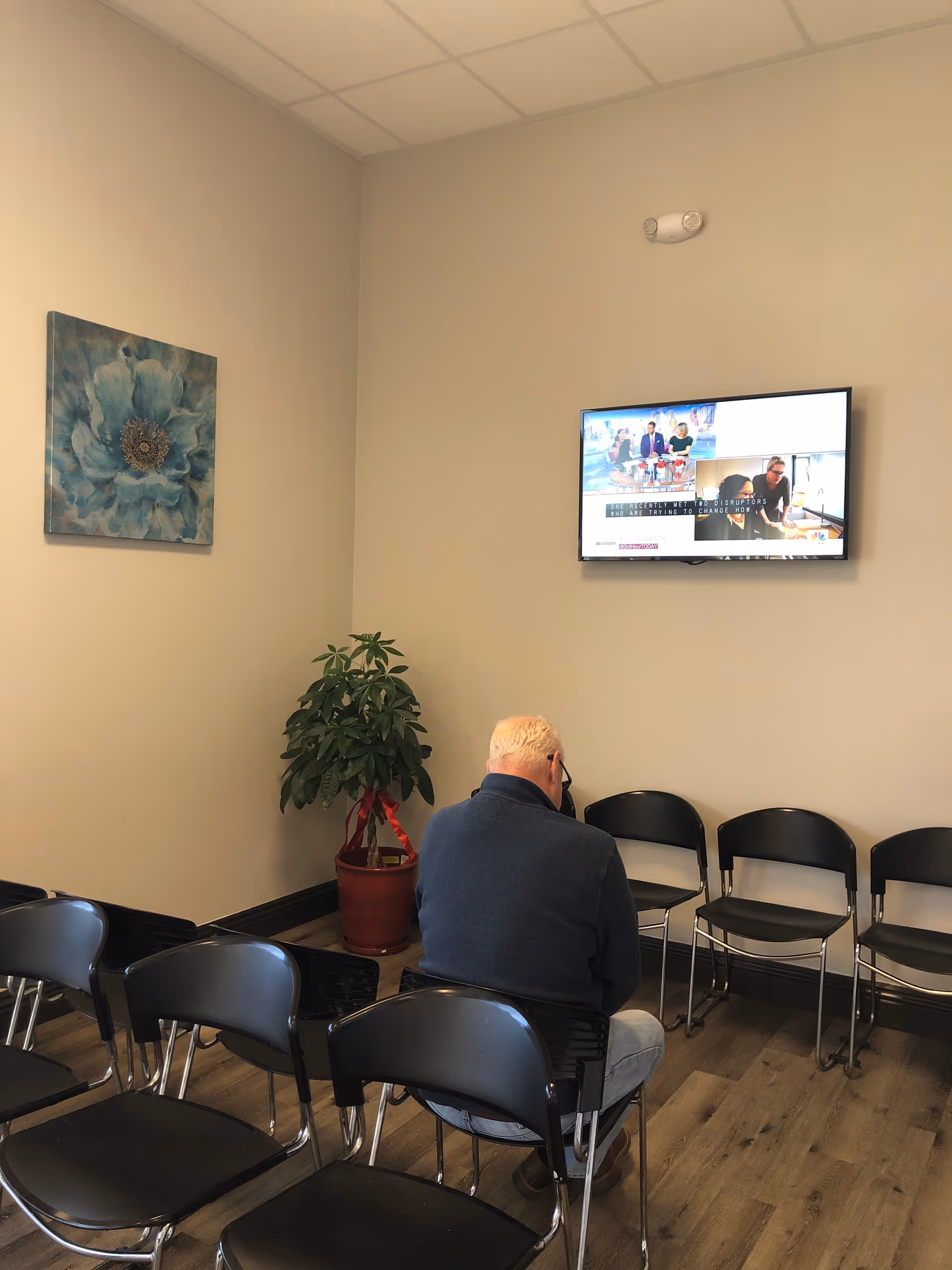 A man sits with his back to the camera in a clinic waiting area with chairs.