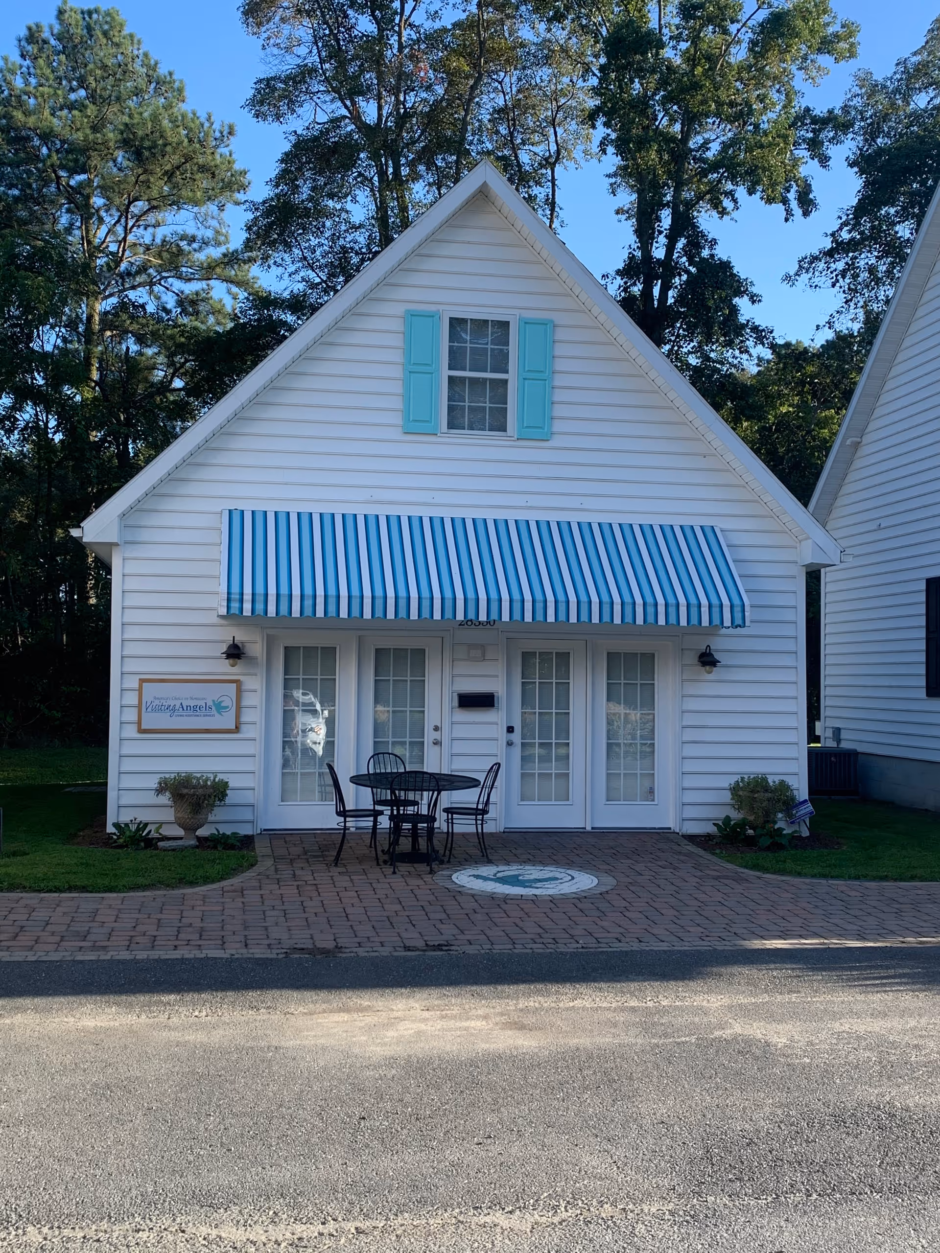 White front of a small building with blue shutters and striped awning, outdoor seating by entrance