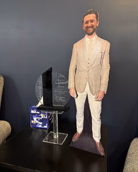 Life-size cardboard cutout of a man beside a trophy on a dark table.
