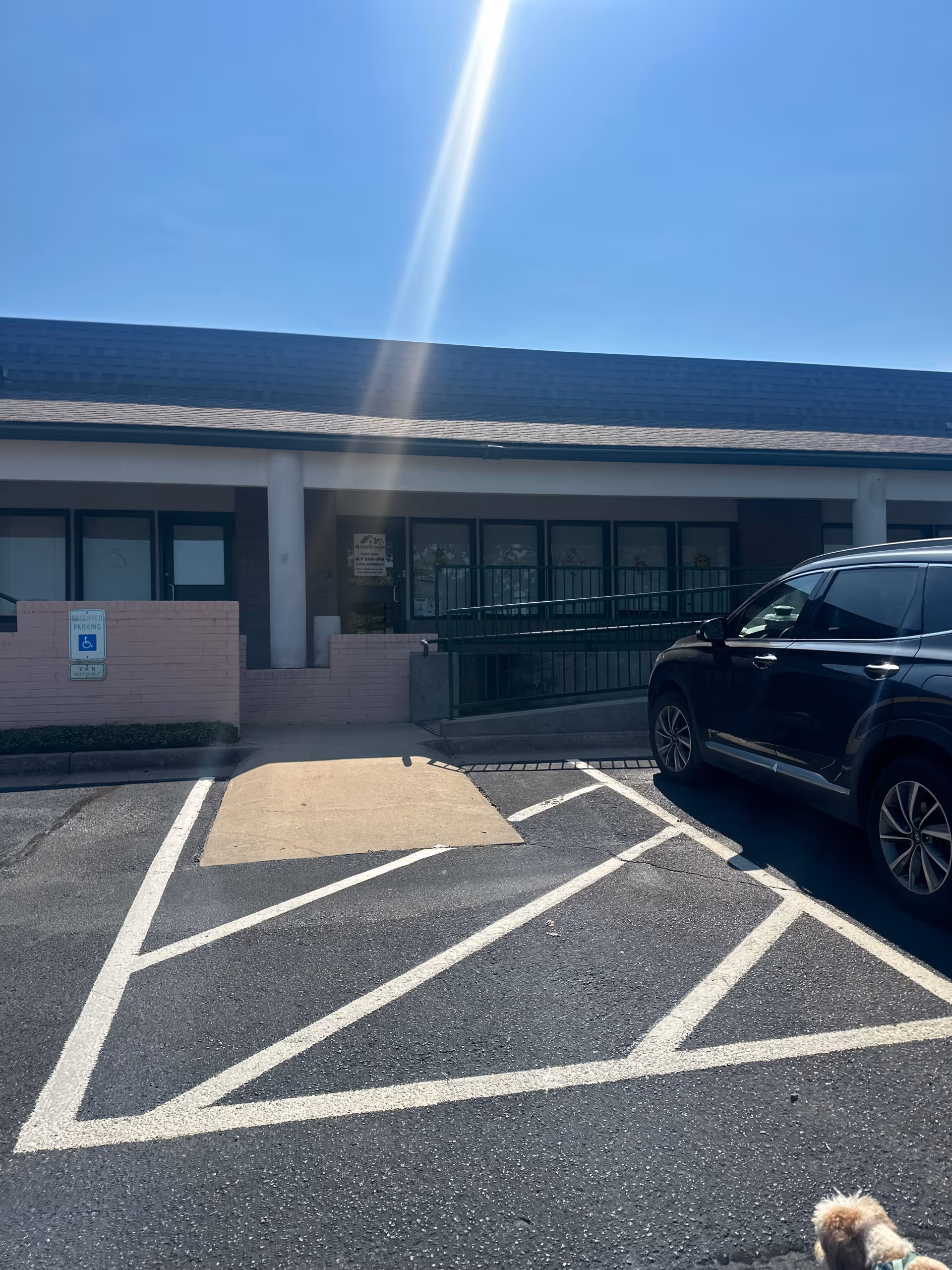 The exterior of a senior care facility with a ramp, parking lot, and a black SUV.