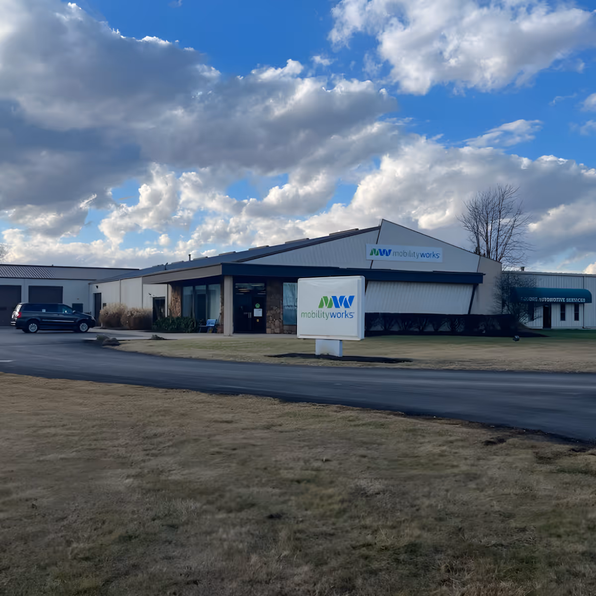 Exterior view of MobilityWorks facility with signage and parked cars under a cloudy sky.