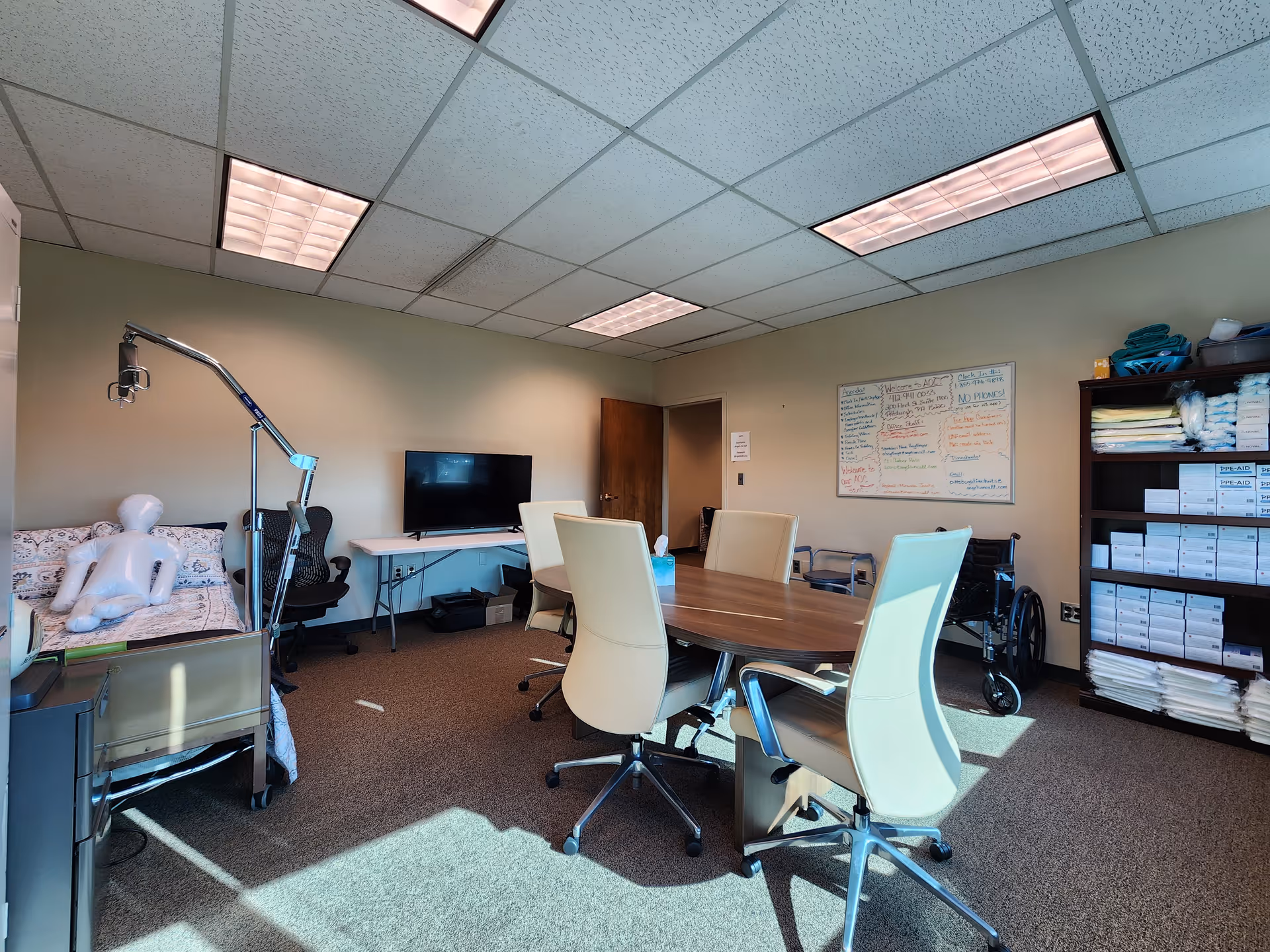 A hospital-style treatment room with a round table, chairs, whiteboard, cabinets, and a bed.