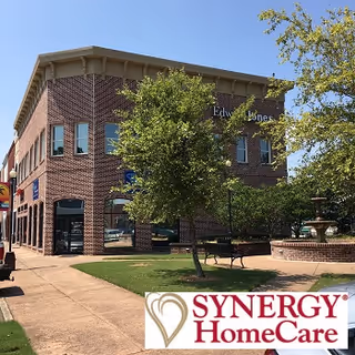 Brick exterior of a Synergy HomeCare building with trees, a fountain, and benches.