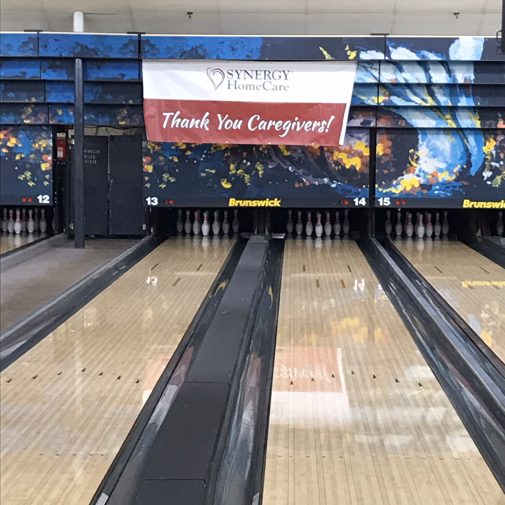 Interior bowling alley with lanes and a SYNERGY HomeCare banner overhead
