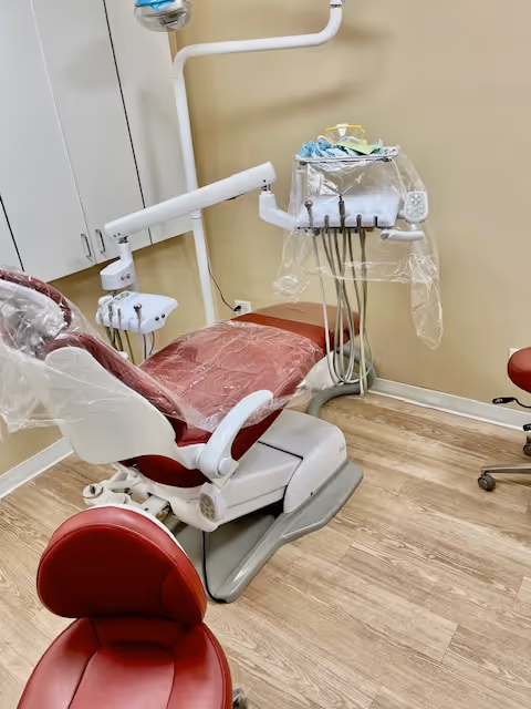 Red dental chair with instrument tray and overhead light in a clinical treatment room.