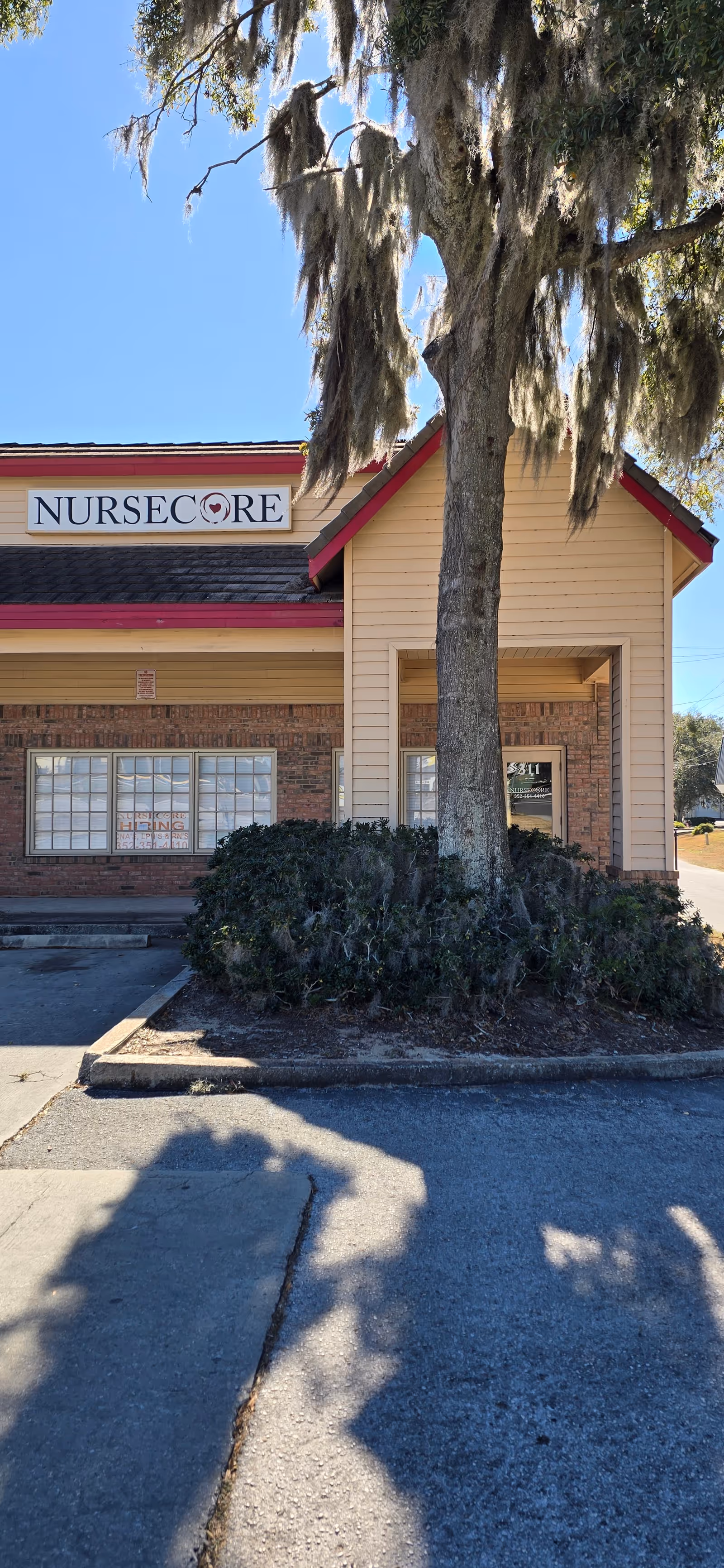 Exterior view of NurseCore senior living facility with sign, entryway, and tree.