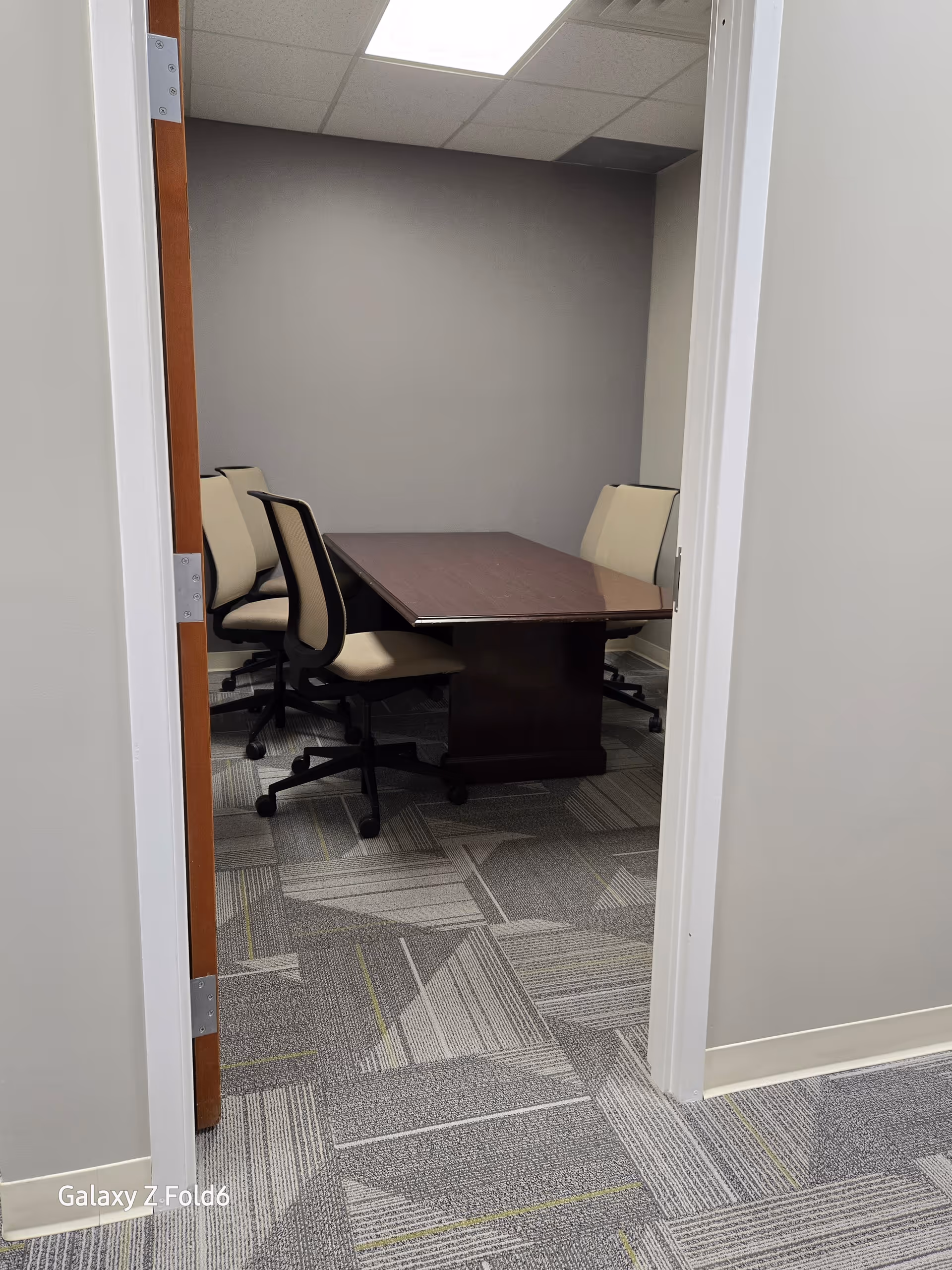 Small conference room with a dark wood table and beige rolling chairs.