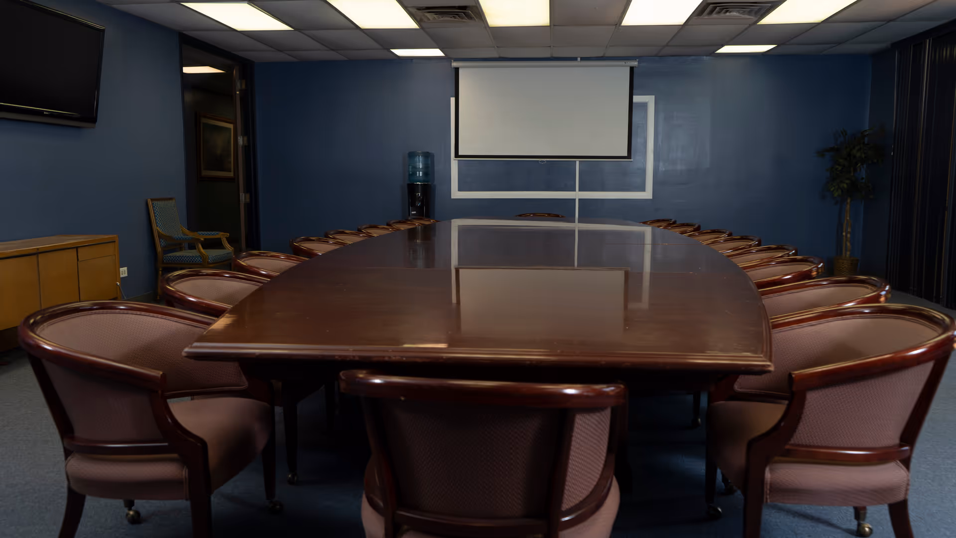 A long wooden conference table with pink upholstered chairs in a blue-walled boardroom.