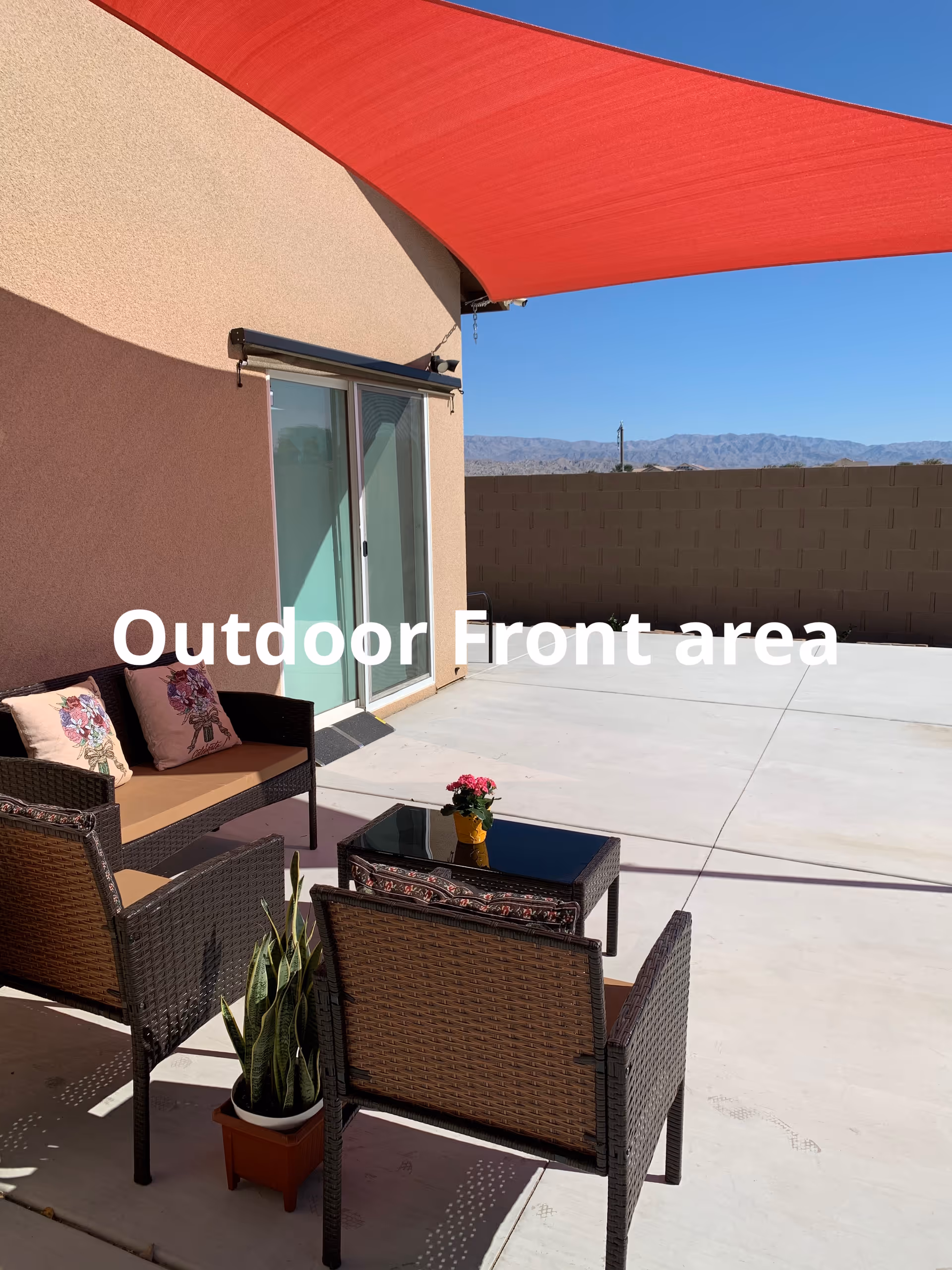Patio seating area outside a retirement home with wicker chairs and a red shade sail.