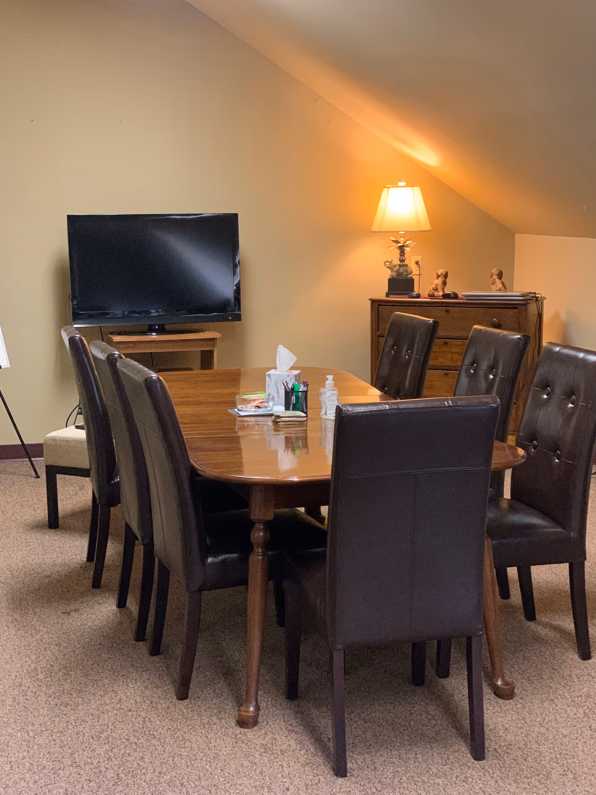 A wooden dining table surrounded by leather chairs in a cozy, dimly lit room.
