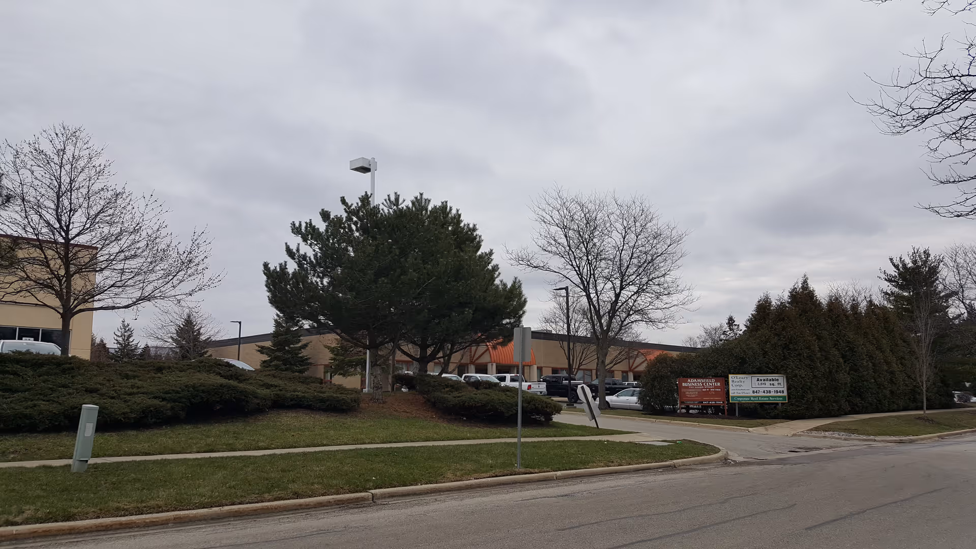 Outdoor view of a LINCARE facility with trees, shrubs, parked cars, and a paved driveway.