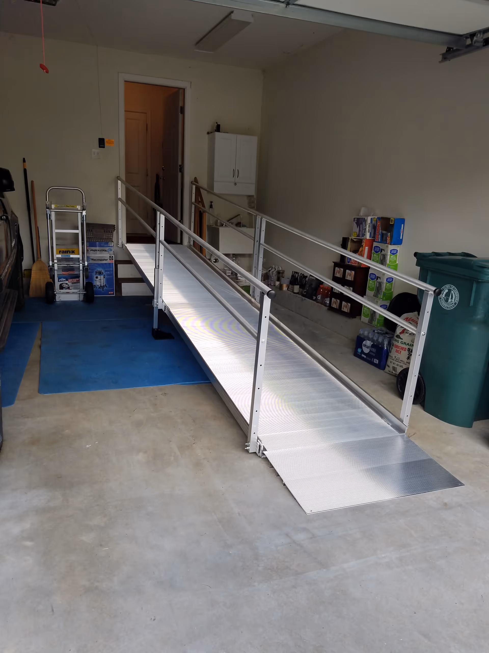Metal wheelchair ramp inside a garage leads to a doorway, with rails on both sides.