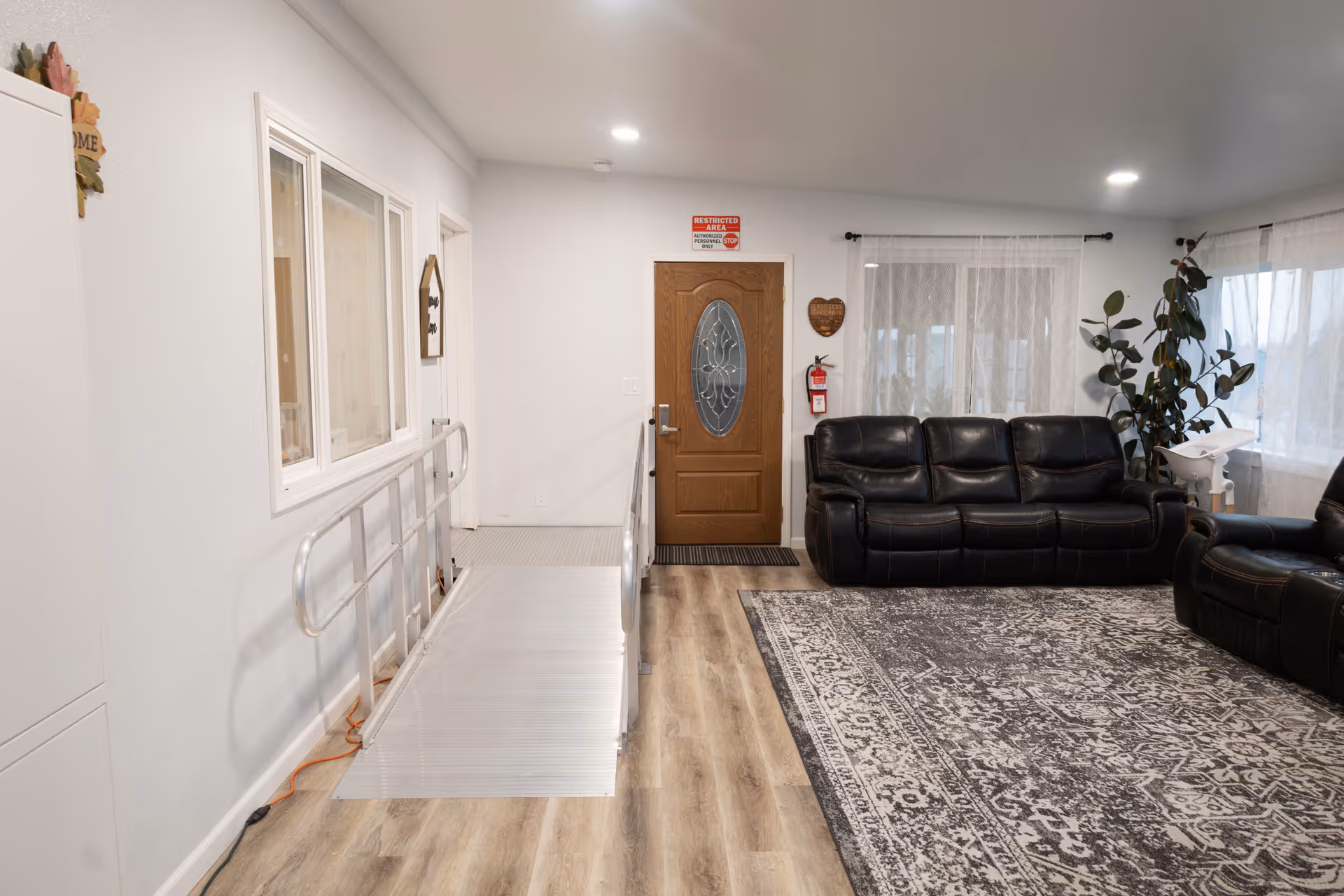 Bright living room with black leather sofas, rug, plants, and a wooden front door.