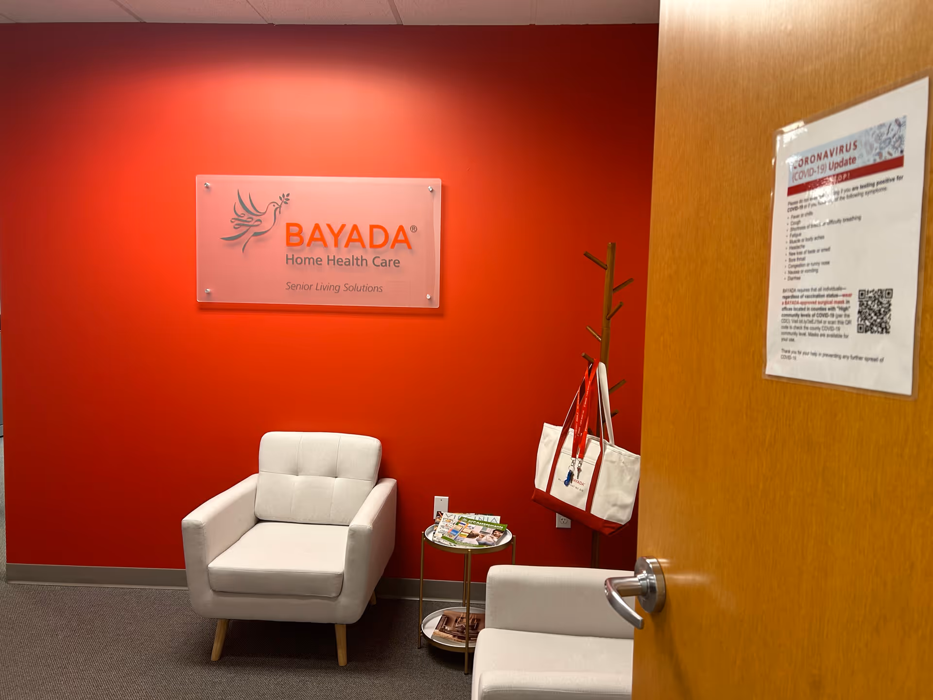 Red-walled waiting area with two white chairs, a side table, and BAYADA sign.