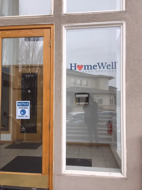 Front entrance of HomeWell Care Services with wooden door and large glass window displaying logo.
