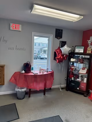 Indoor room with pink round table, balloons, and a trophy cabinet near an exit.