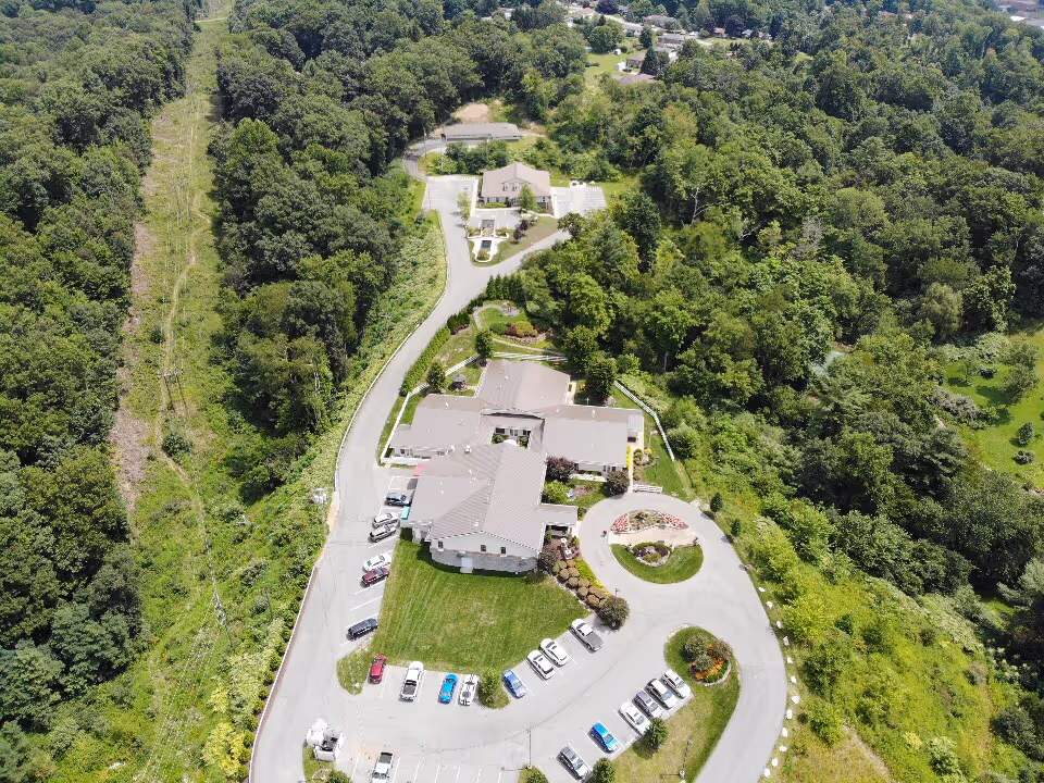 Aerial view of a hospice facility surrounded by trees, with a circular driveway and parking.