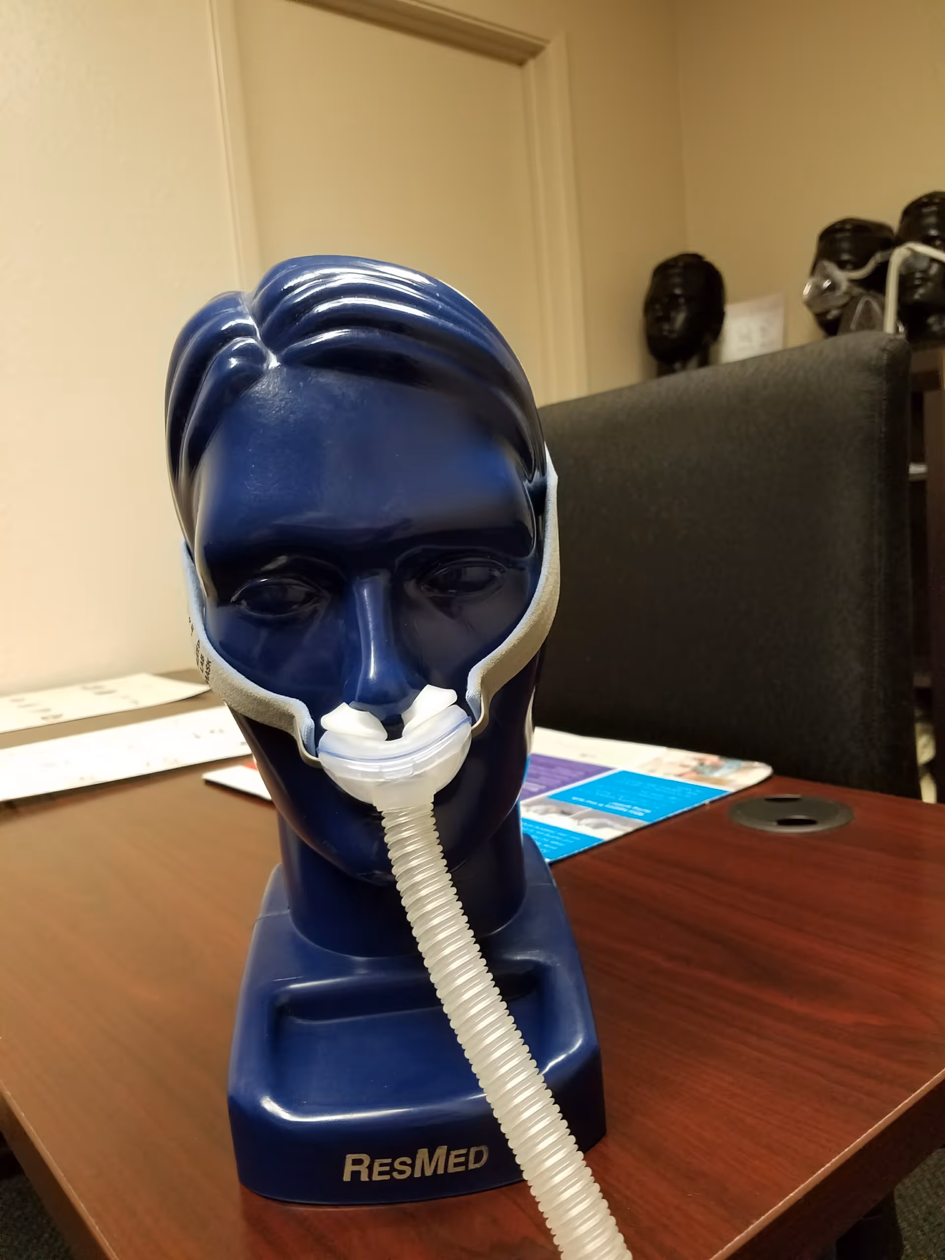 Blue mannequin head wearing a CPAP mask on a wooden table in an office.