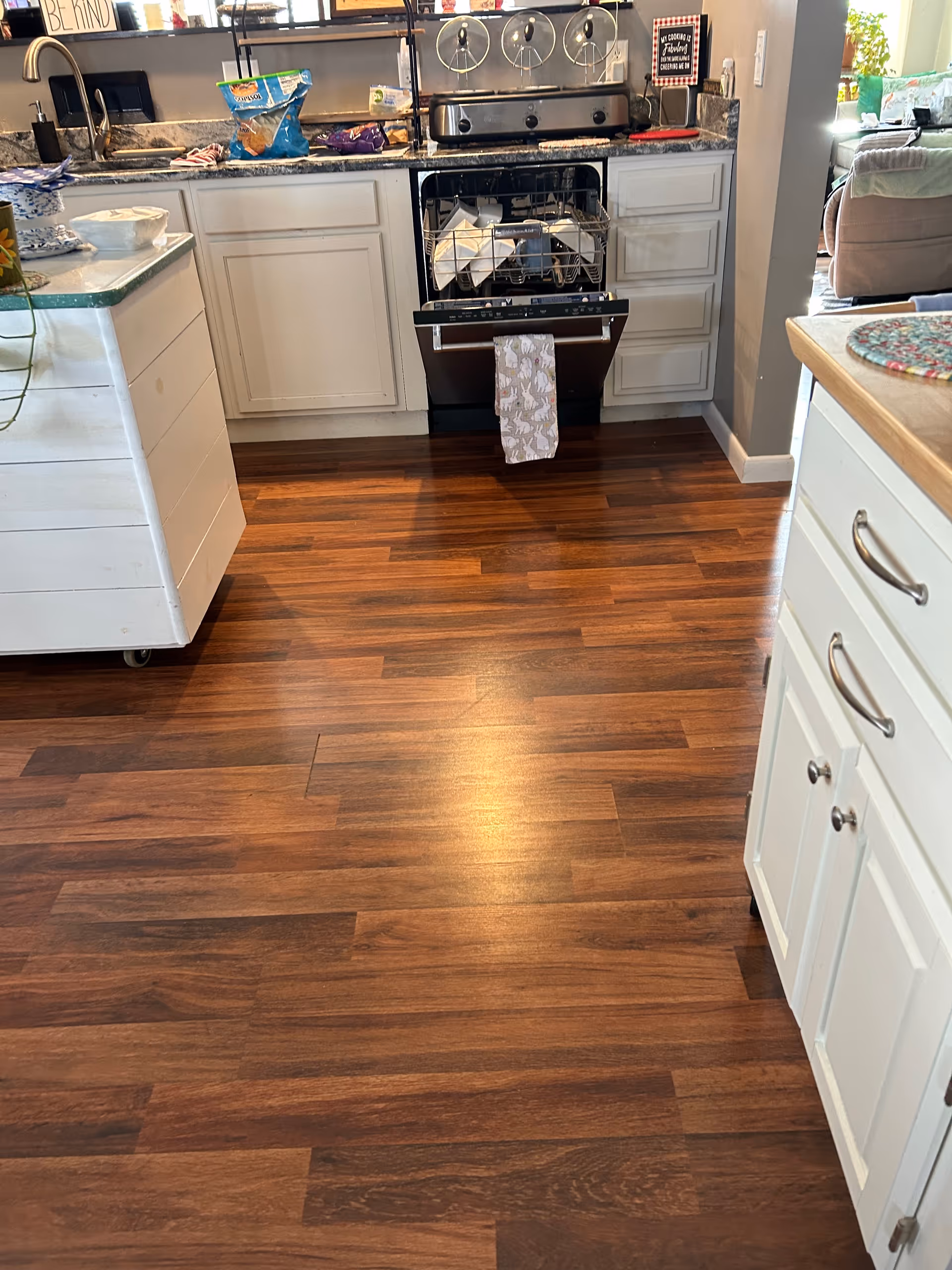 Kitchen scene with open dishwasher, white cabinets, and rich wood flooring.
