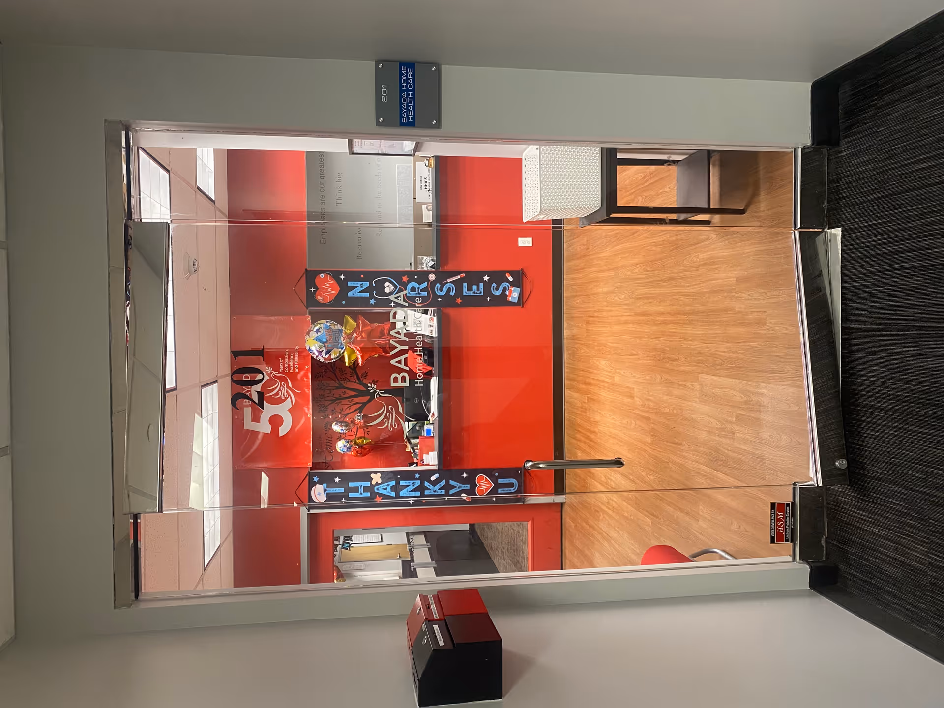 Entrance to a BAYADA facility hallway with glass doors, red decor, and seating.