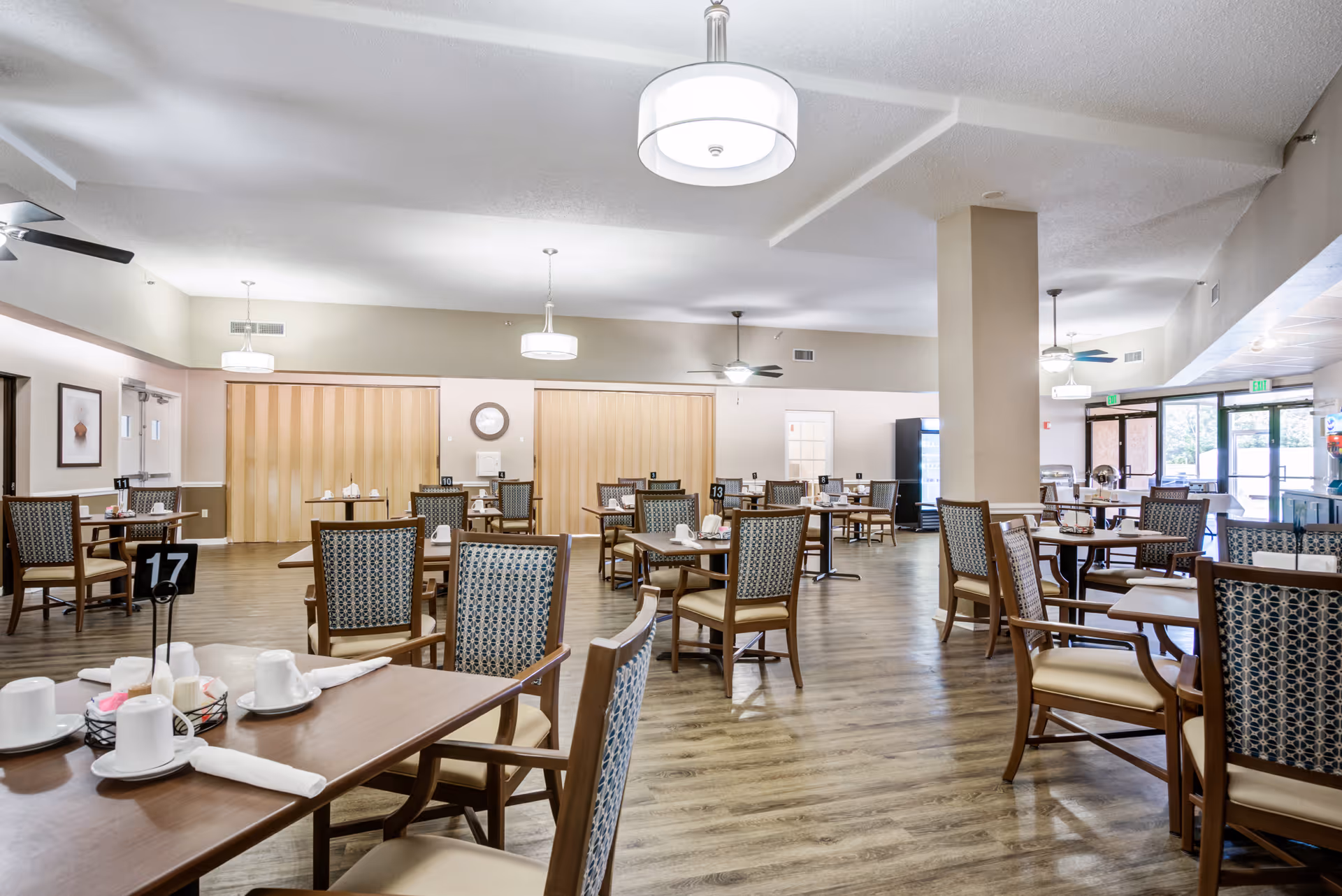 Bright senior living dining room with multiple tables, chairs, and place settings.