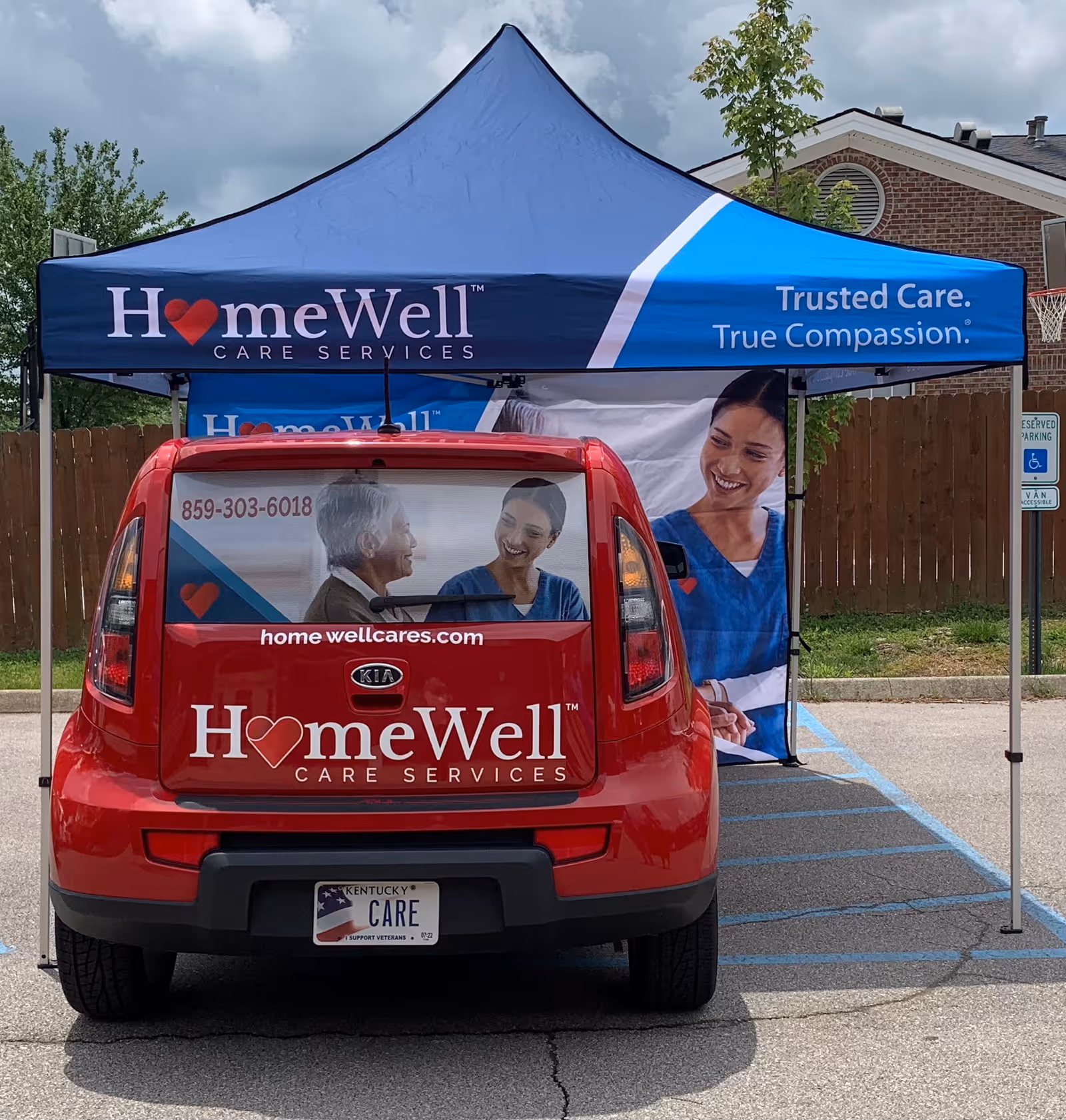 Red HomeWell Care Services van parked under a blue promotional tent in a parking lot.
