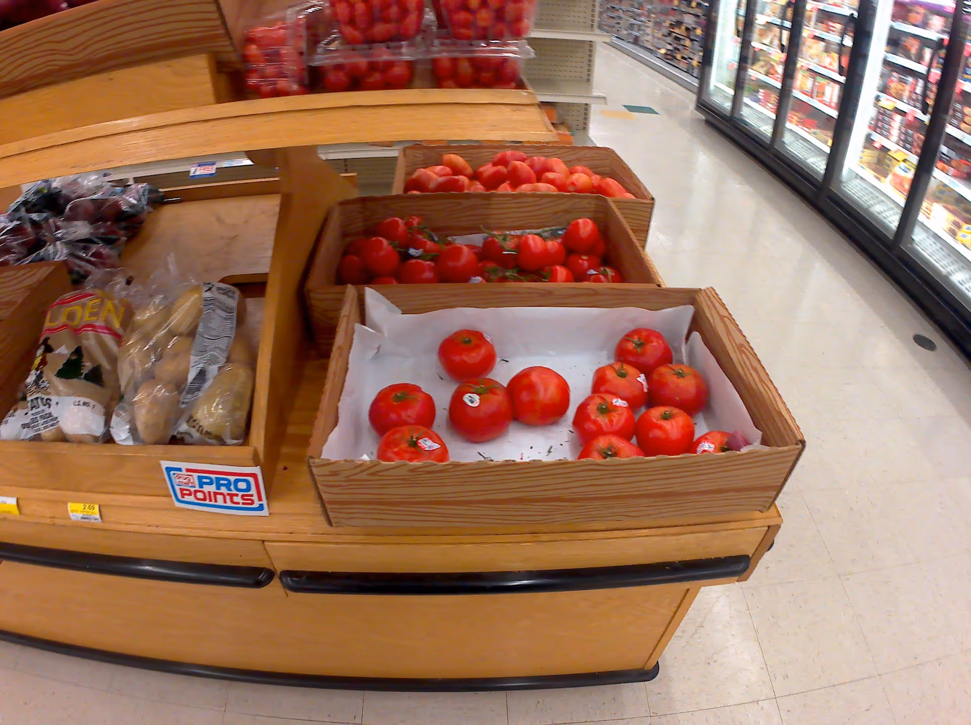 Wooden crates hold red tomatoes in a grocery-store produce section.