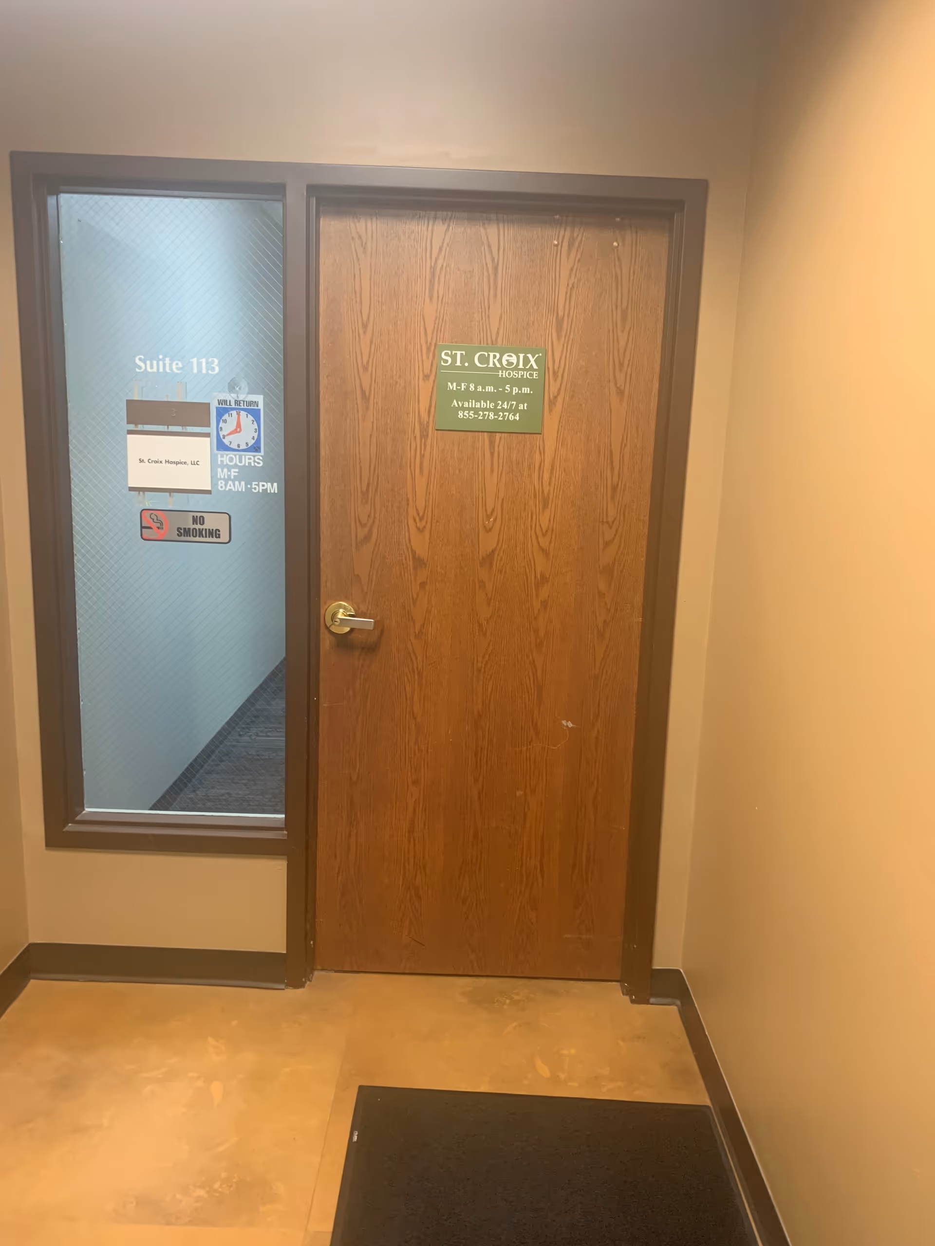 Interior hallway with wooden door labeled St. Croix Hospice and adjacent glass window.