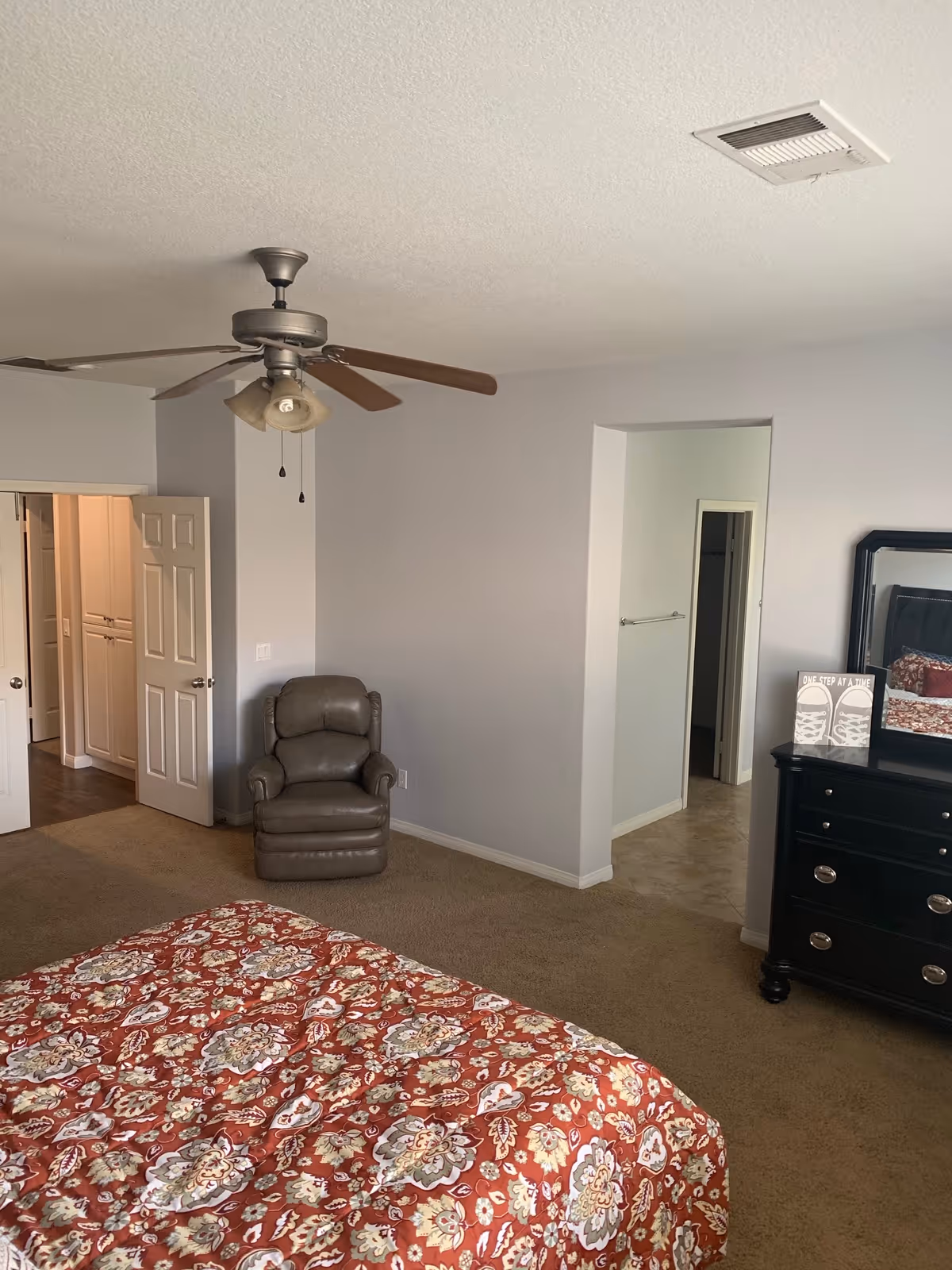 Bedroom in a senior living facility with a bed, recliner, dresser, and ceiling fan.