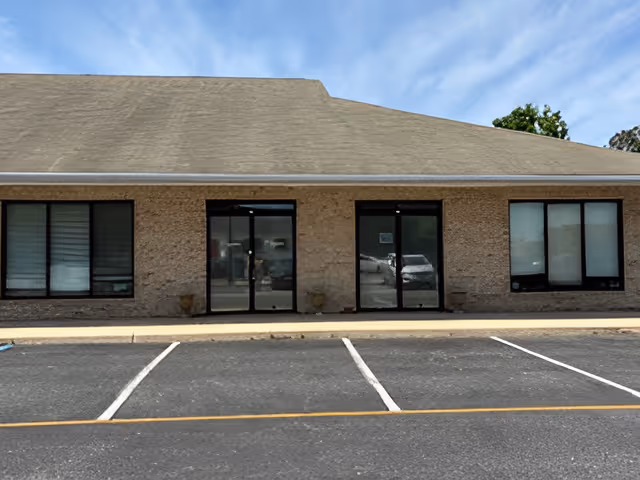 Single-story brick building with glass doors and a parking lot in front.