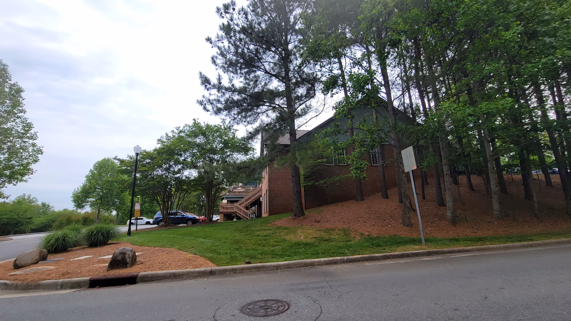 Exterior view of a brick facility with trees, parked cars, and a wooden staircase.