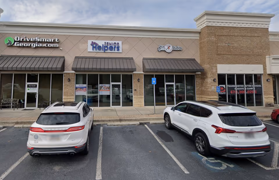Exterior view of a strip mall with Senior Helpers storefronts and parked cars.