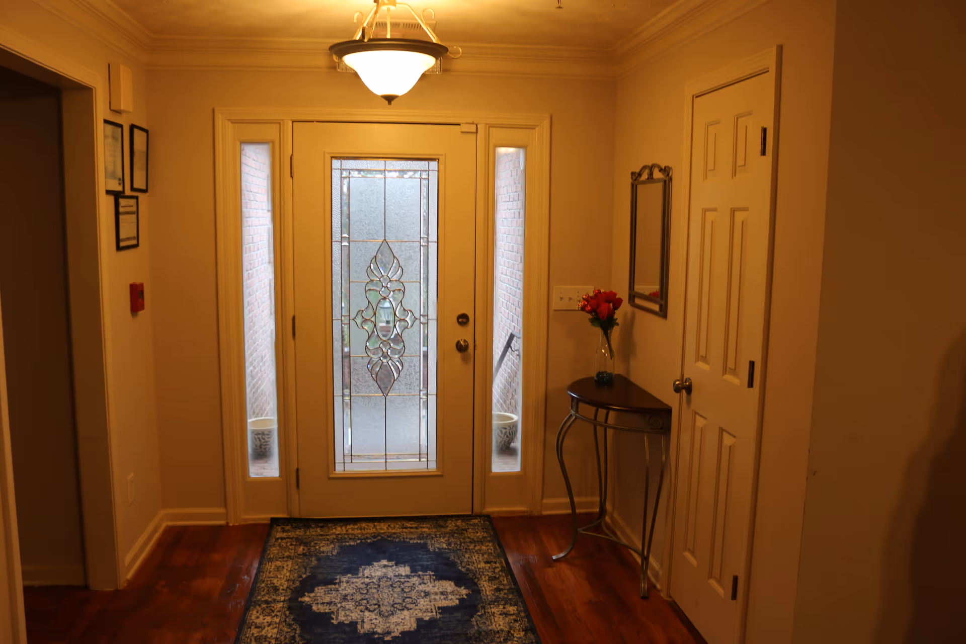 Hallway entry with stained-glass front door, side windows, rug, and vase on a table.