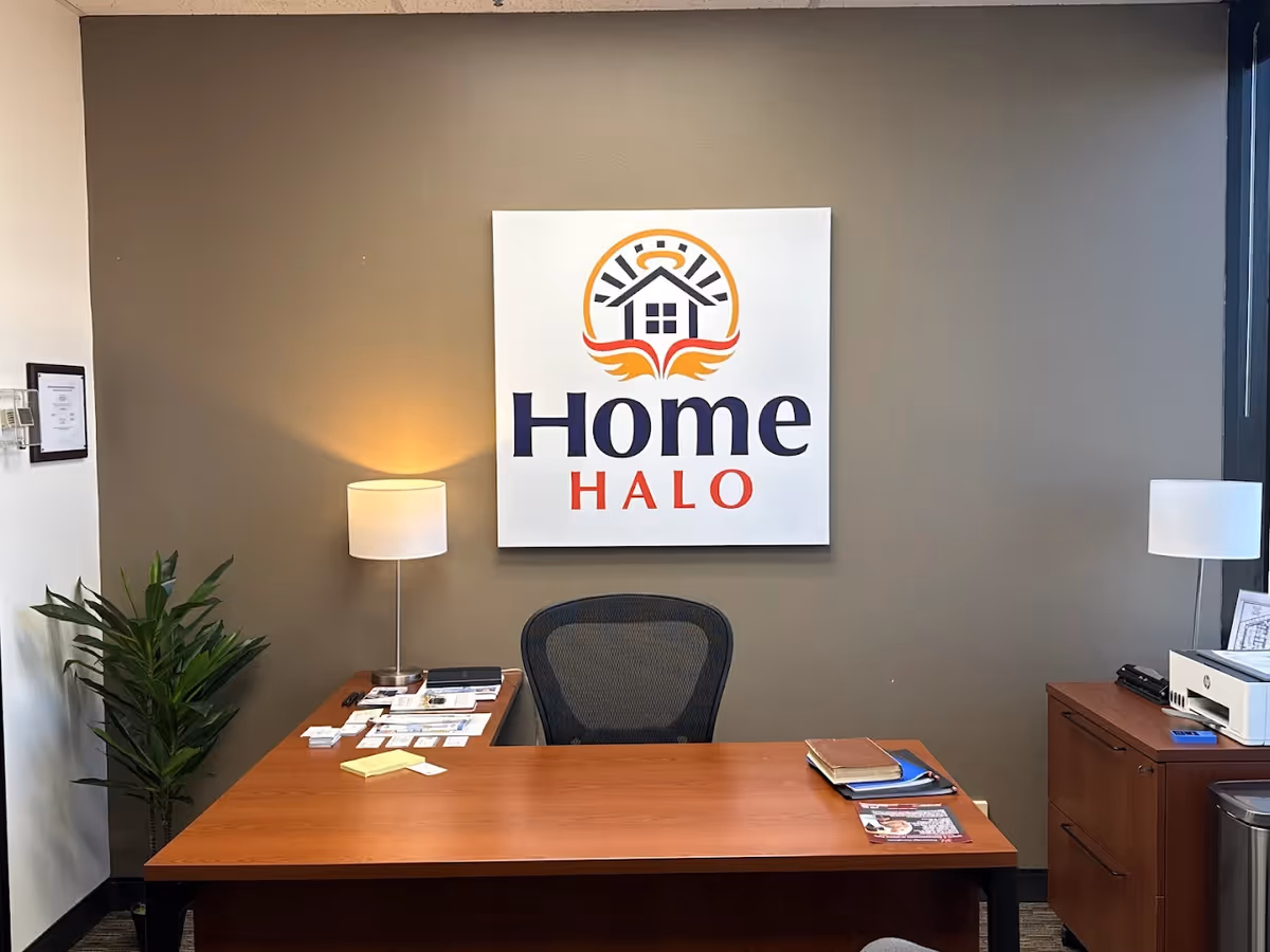 Reception area with a large Home Halo sign on a gray wall behind a wooden desk.